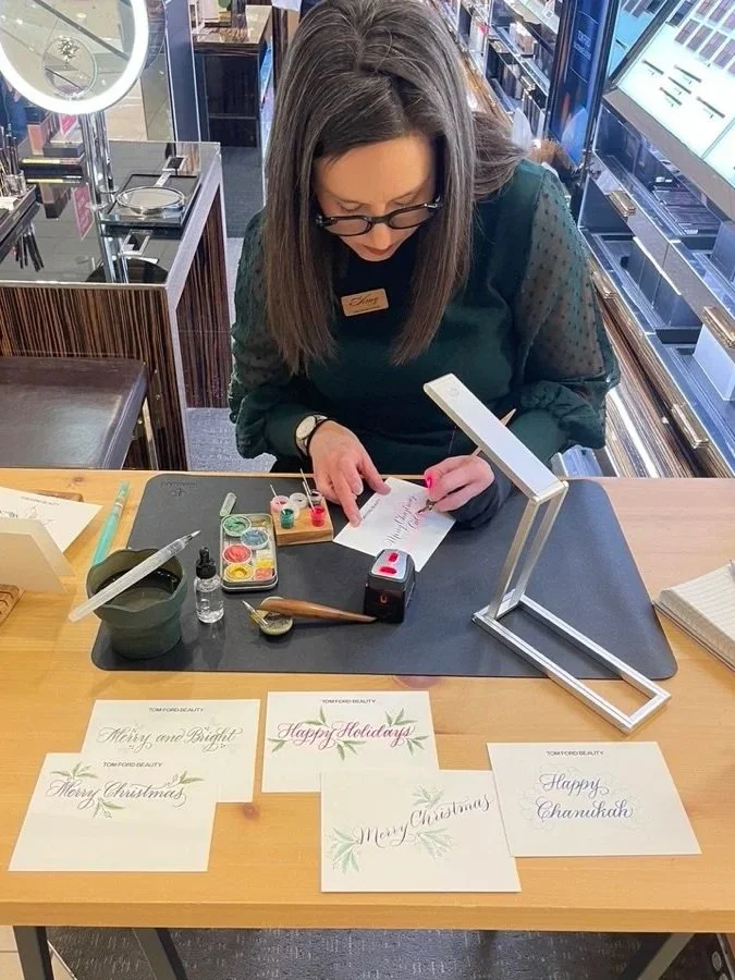 Woman at a jewelry store creating holiday greeting cards with calligraphy and watercolor paints.
