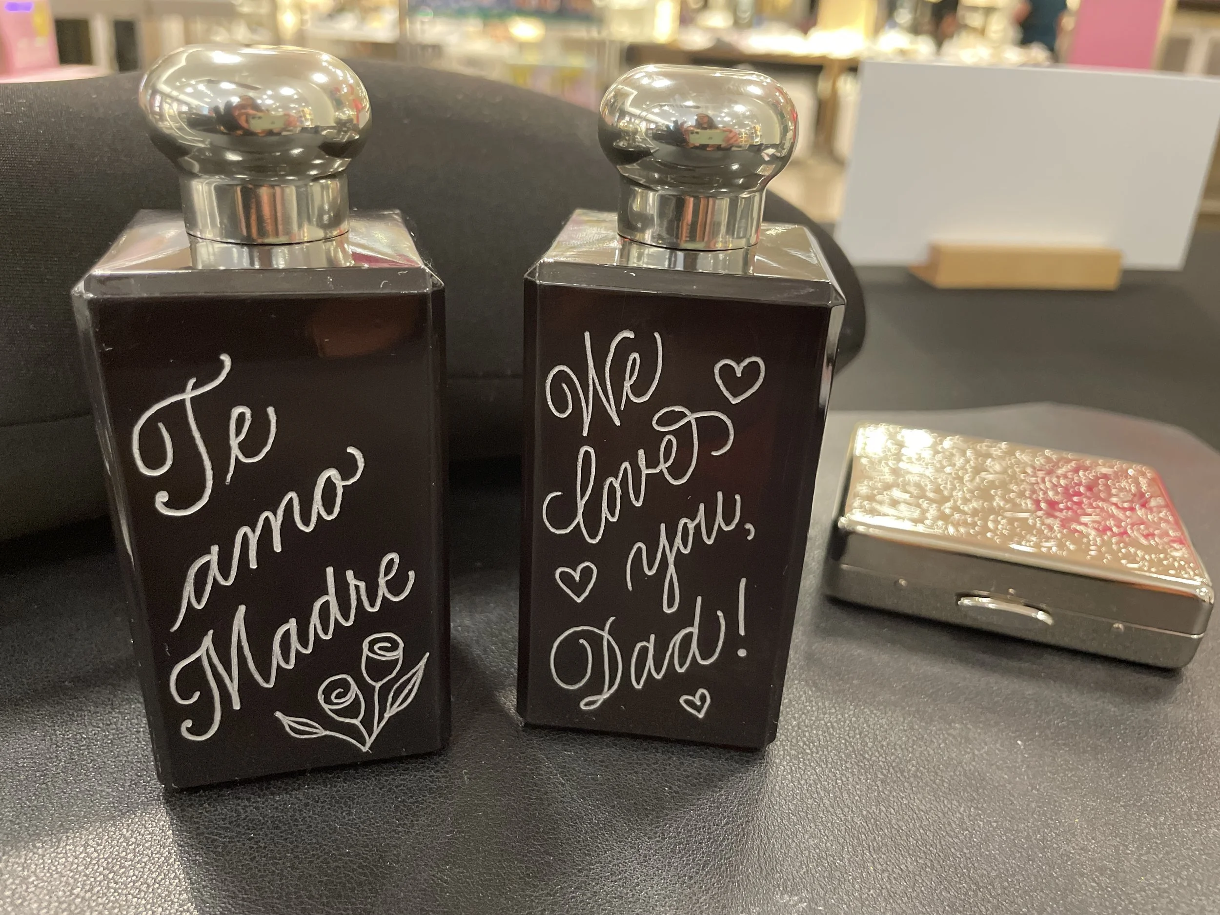 Decorative perfume bottles with handwritten messages for Mother's Day and Father's Day, placed on a retail display table.