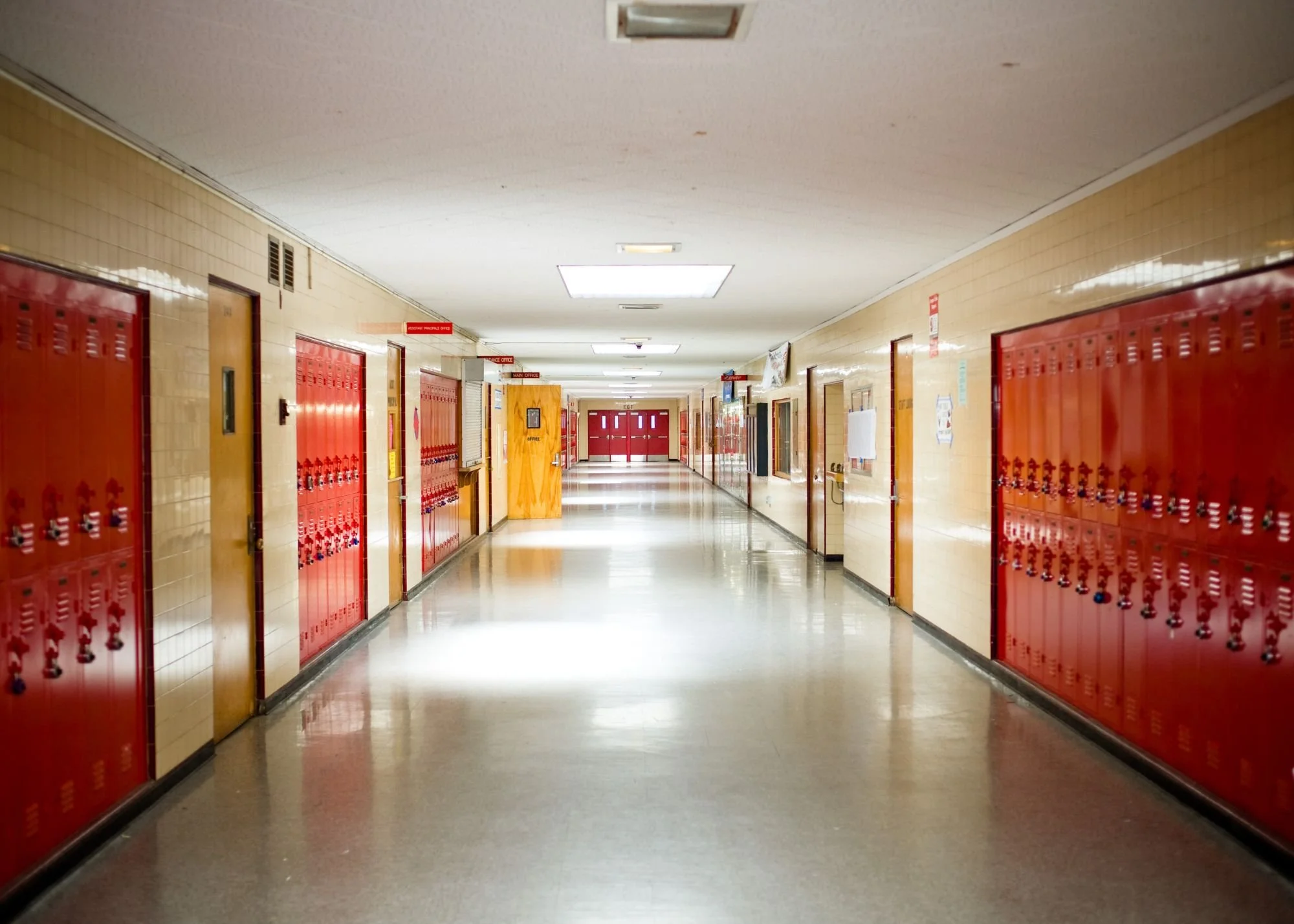 Empty school hallway with red lockers and closed classroom doors.