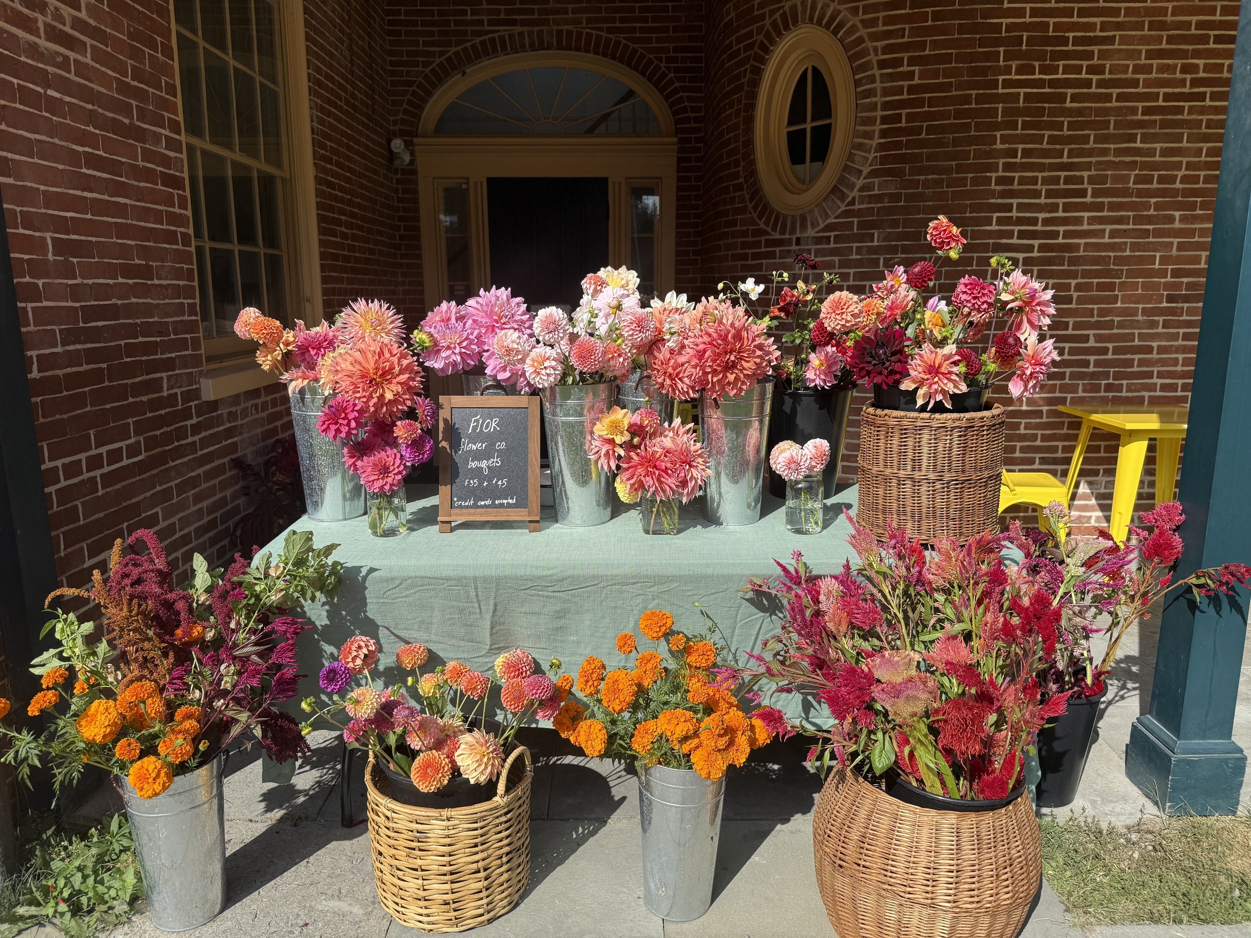 Elegant, abundant, whimsical vases of multi-colored ranunculus flowers set up on a table at a pop-up market at Farmer & Co. in Unionville, PA.
