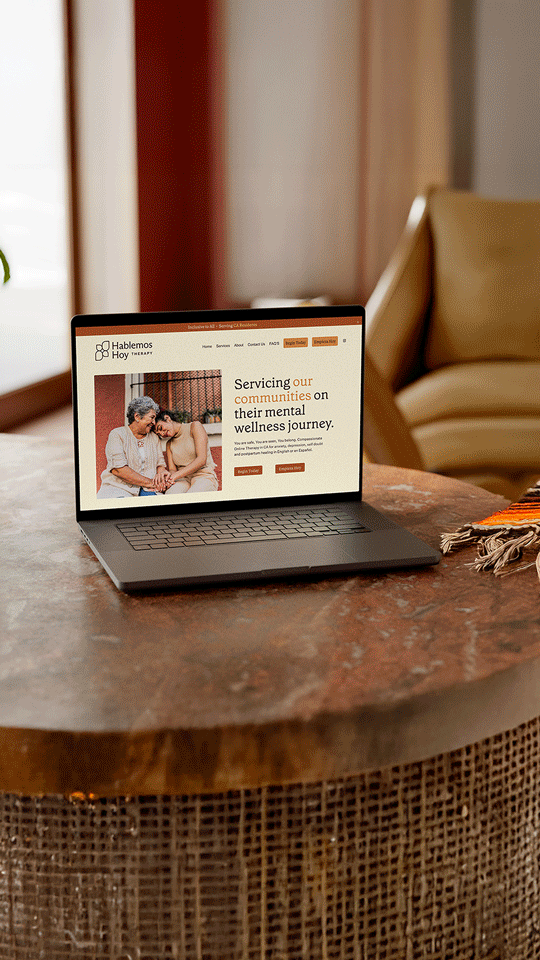 A laptop on a round wooden table displaying a website about mental wellness services for communities.