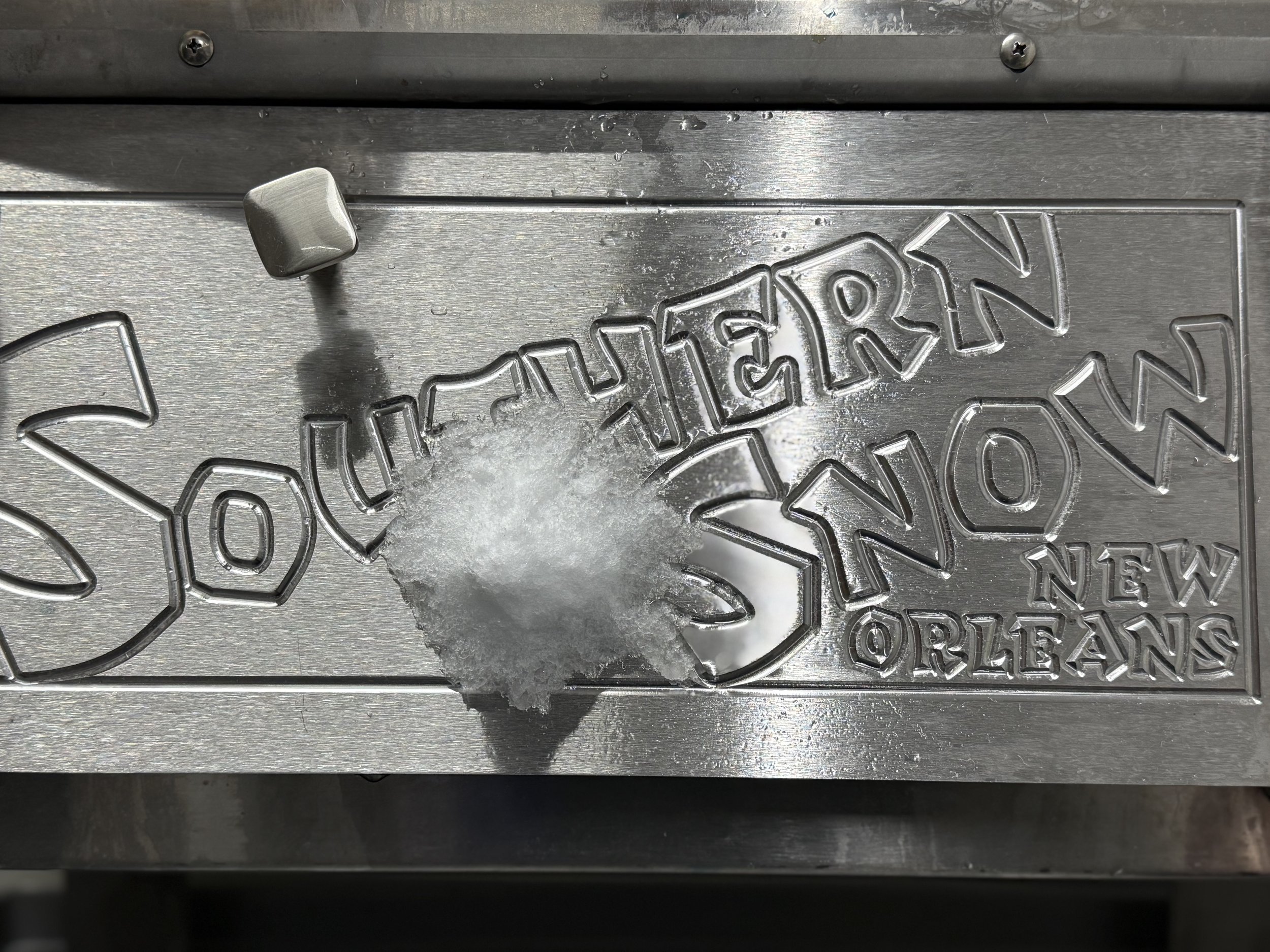 A metal sign with the text 'SOUVLAKEN', 'NEW ORLEANS', and the letter 'S' is broken, revealing ice and a small paddle.