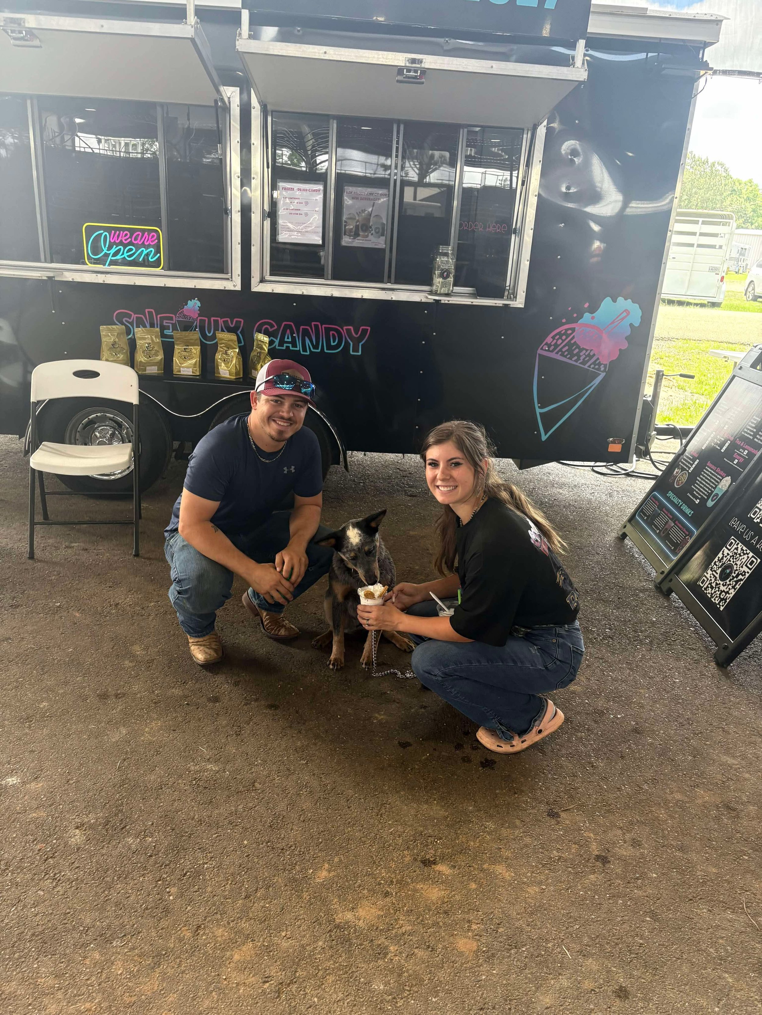Two people and a dog at a rainbow-colored ice cream truck, smiling and holding ice cream cones.