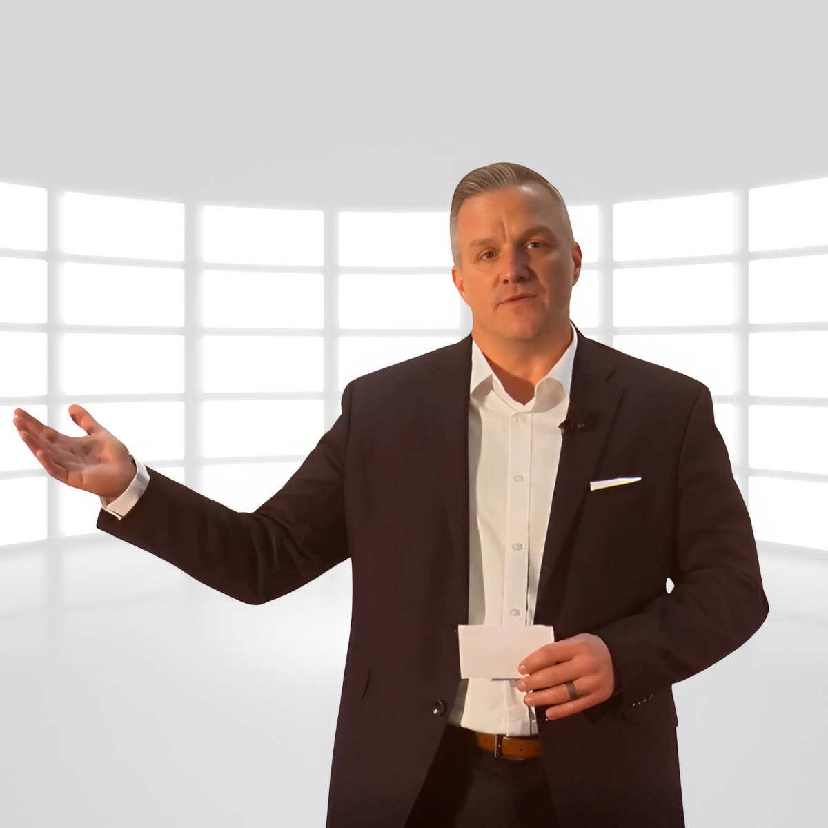 A man in a black suit and white shirt holding a note, standing in front of a bright, futuristic, grid-patterned background.