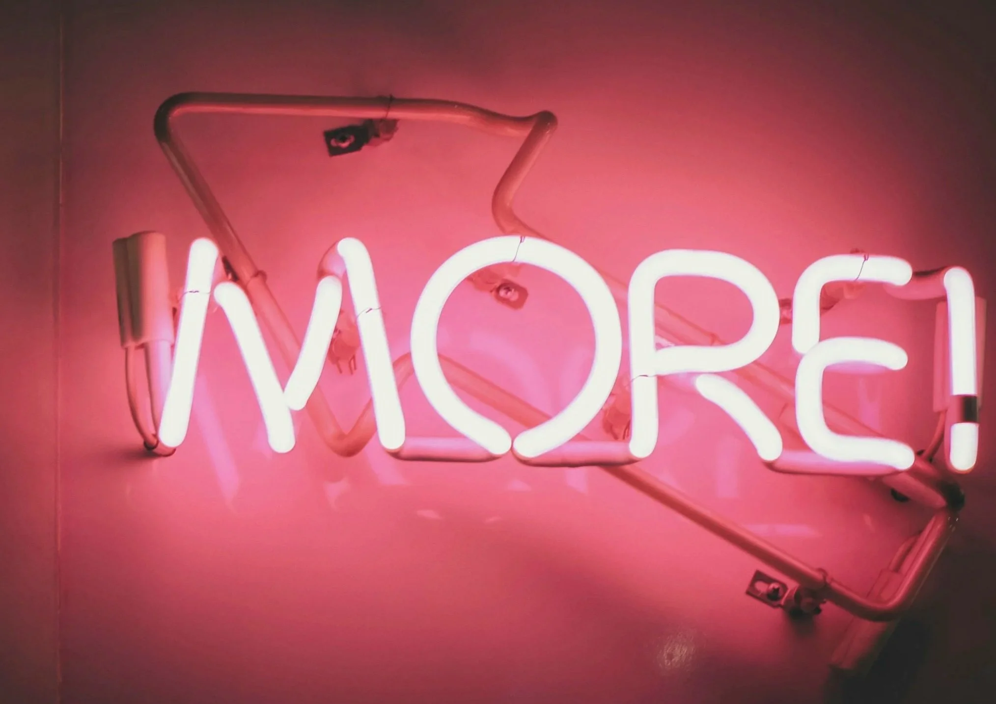 Pink neon sign spelling 'MORE' mounted on a wall