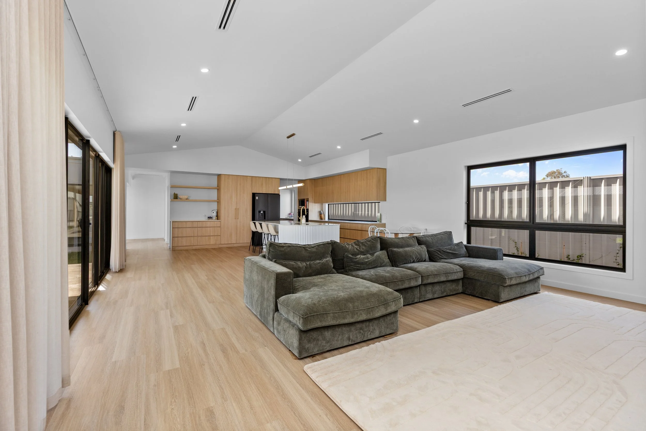 Modern open-concept living room and kitchen with wood flooring, large window, gray sectional sofa, and neutral decor.