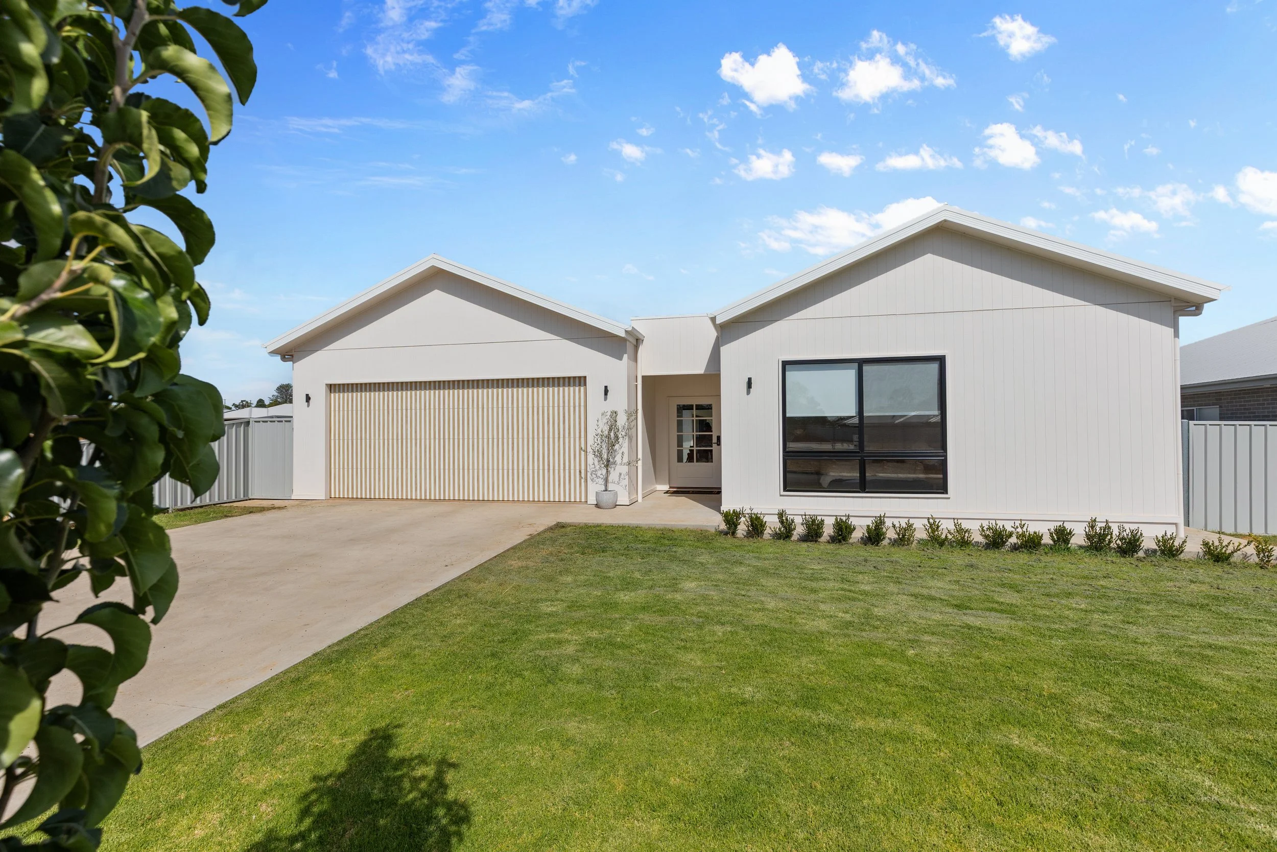 Modern white house with a double garage, large front window, and a well-maintained lawn.