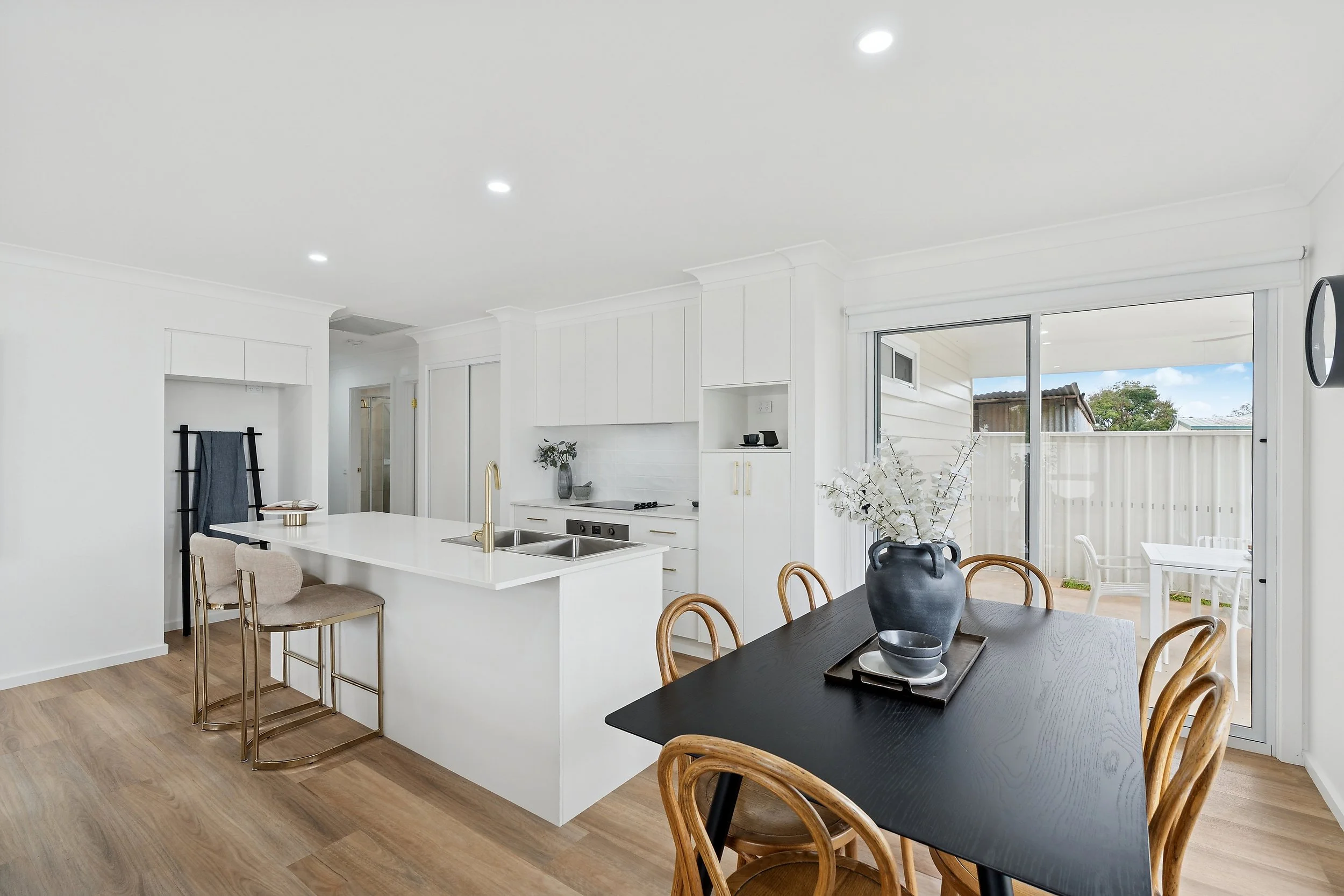 Modern kitchen and dining area with white cabinetry, a black dining table with wooden chairs, and sliding glass doors leading to an outdoor patio with white furniture.