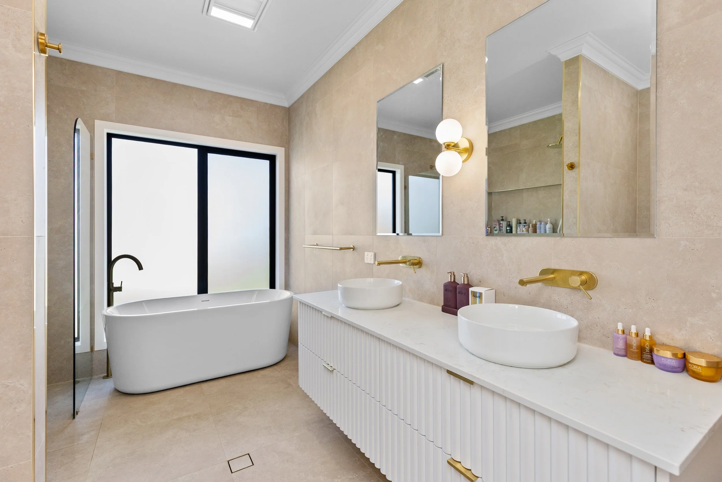 Modern bathroom with a freestanding bathtub, double vanity with vessel sinks, large mirrors, and a frosted window.