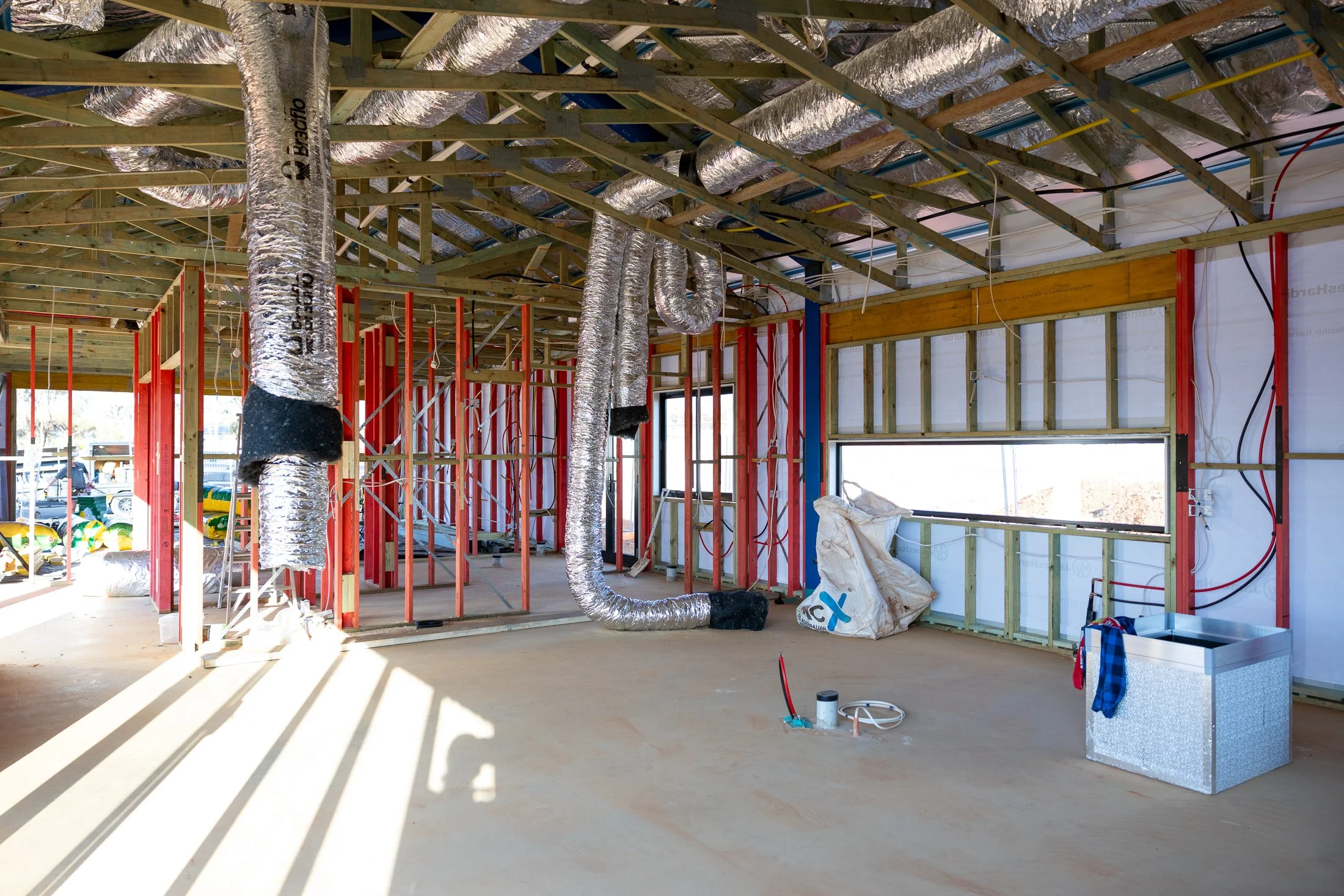 Interior view of a house under construction with exposed wooden framing, ventilation ducts, and unfinished walls.