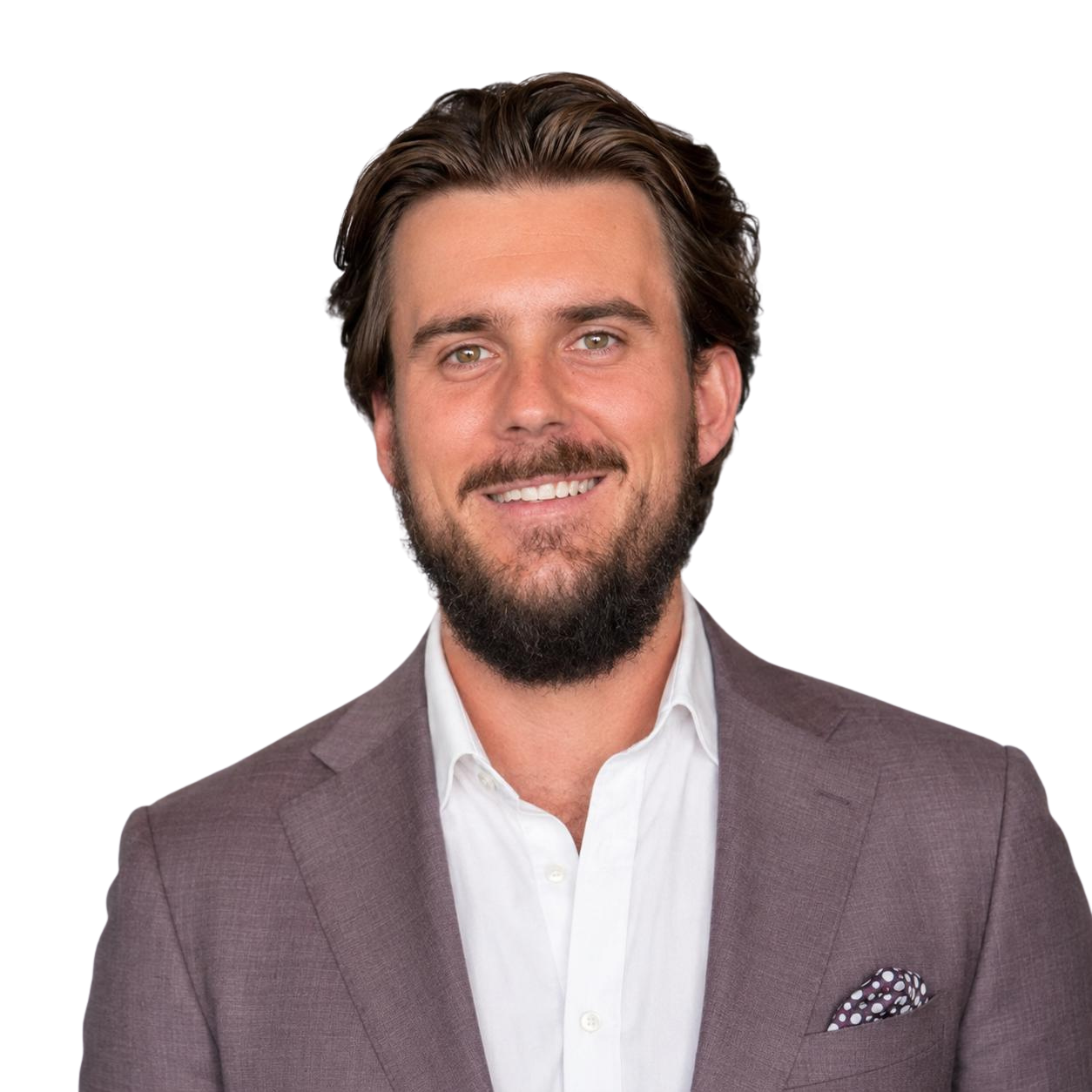 A young man with brown hair, a beard, and blue eyes, smiling, dressed in a black shirt and tan blazer, standing against a plain background.