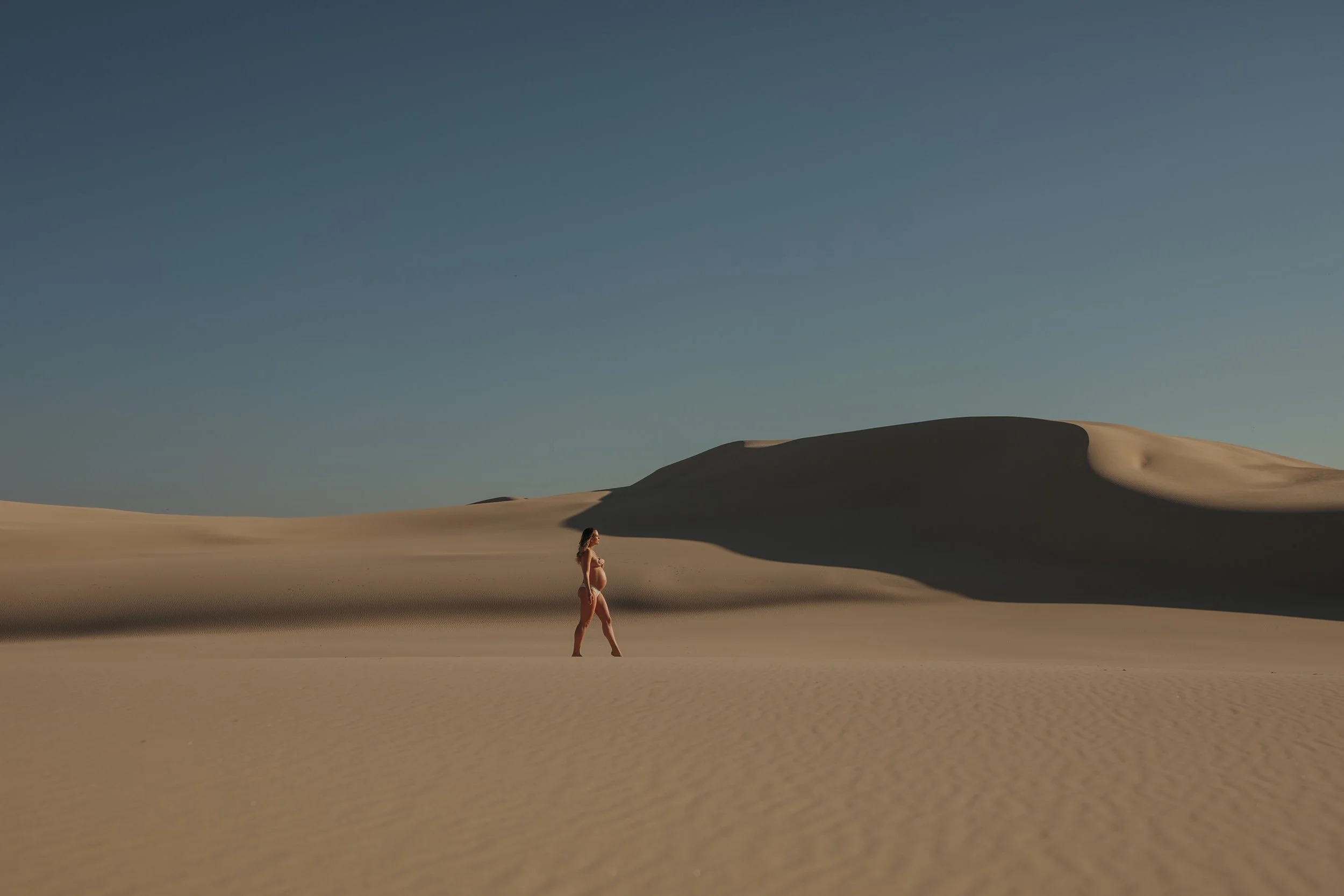 Maternity photoshoot, of an expecting mum, walking nude amoungst sand dunes, during a creative photoshoot, showcasing her bump