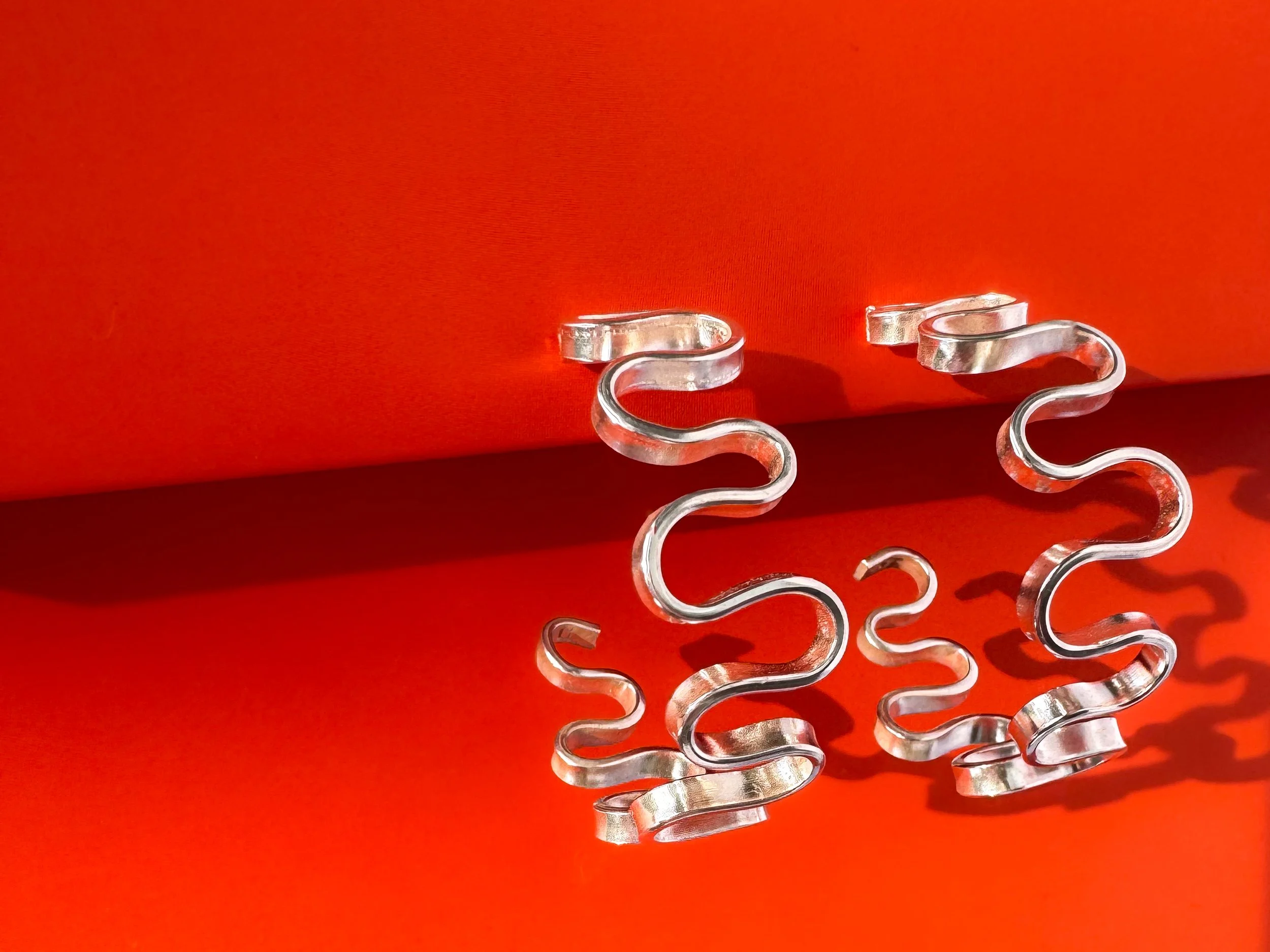 Salome wavy hoop earrings handcrafted in fine silver on a bright coral background