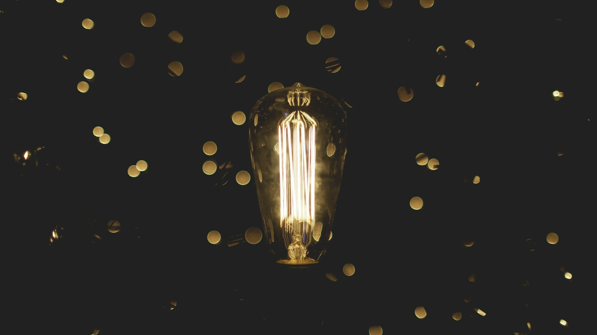 A glowing incandescent light bulb against a dark background with blurred lights.