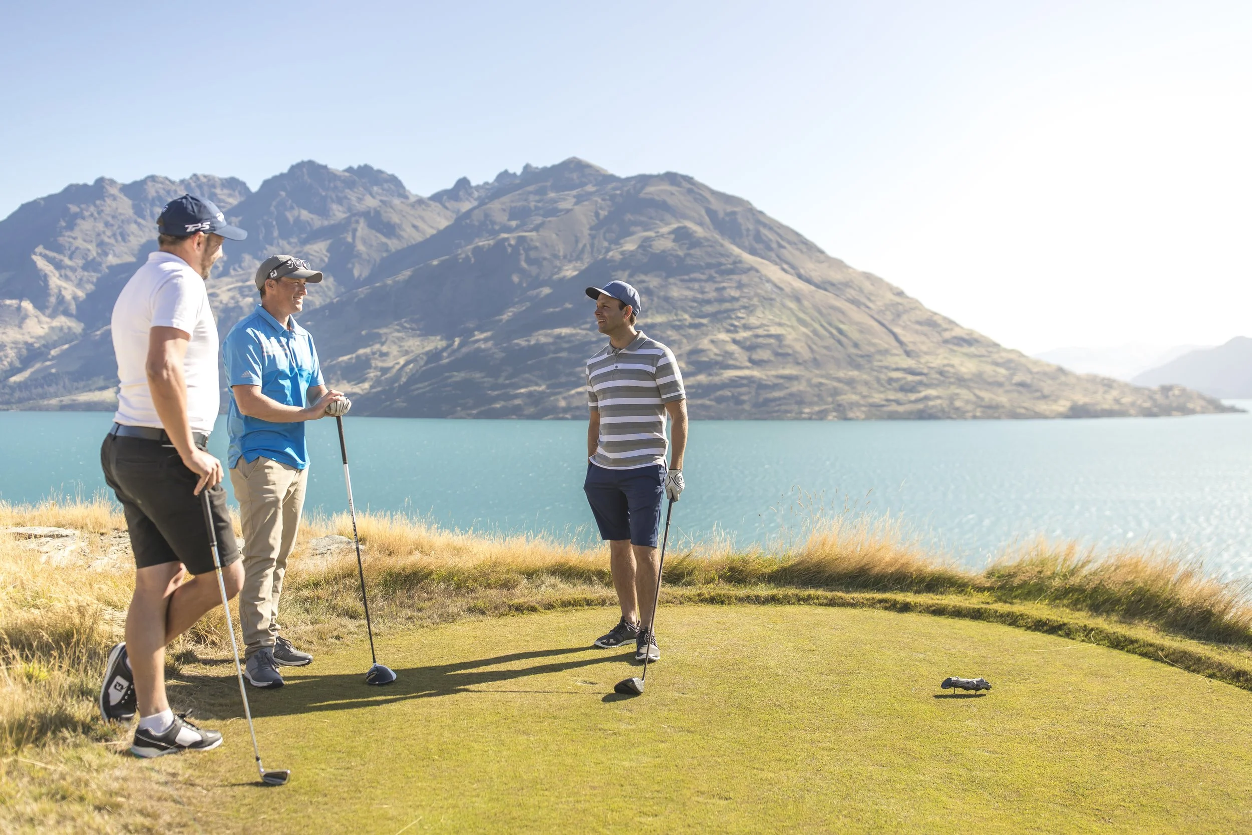 Three men playing golf with lake and mountains in background