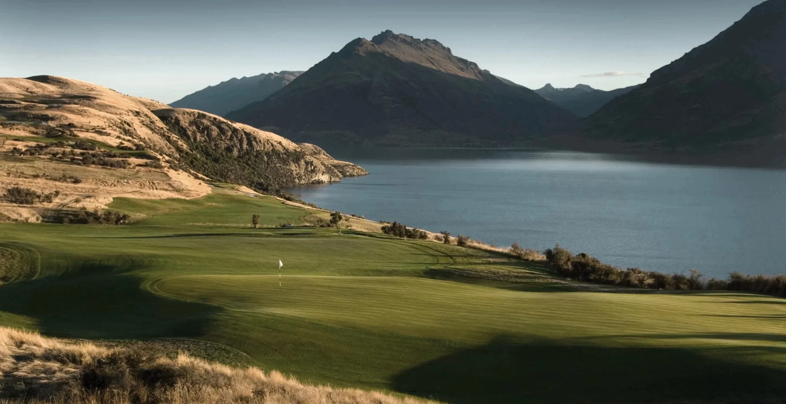 Scenic landscape with golf course, lake, and mountains under a clear sky.