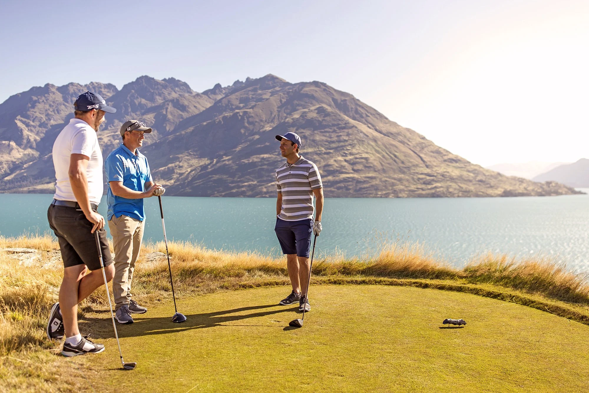 Three men playing golf with mountain and lake view