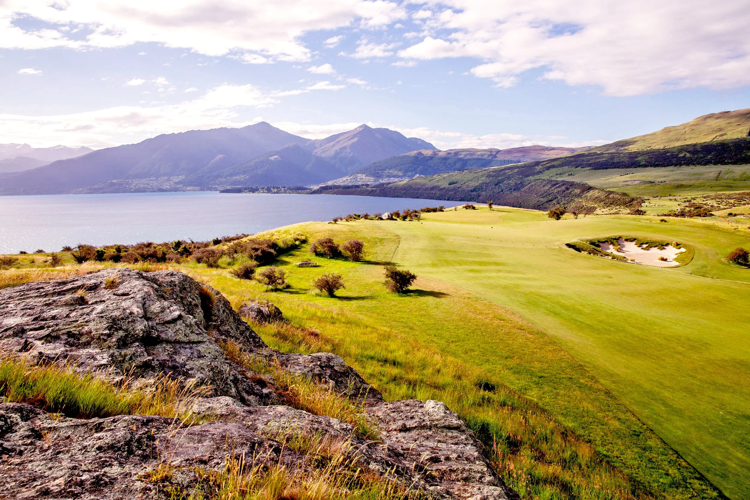 Scenic golf course by mountain lake with clear sky