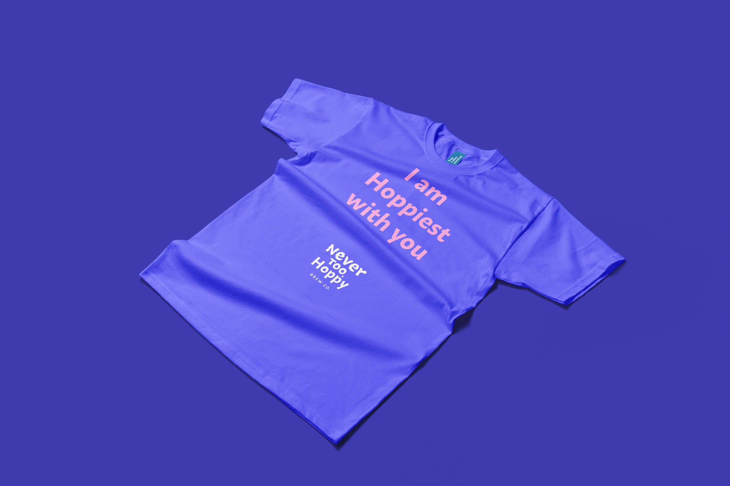 A purple T-shirt with the message "I am Hoppiest with you. Never Too Happy" printed in pink and white text, lying on a purple background.