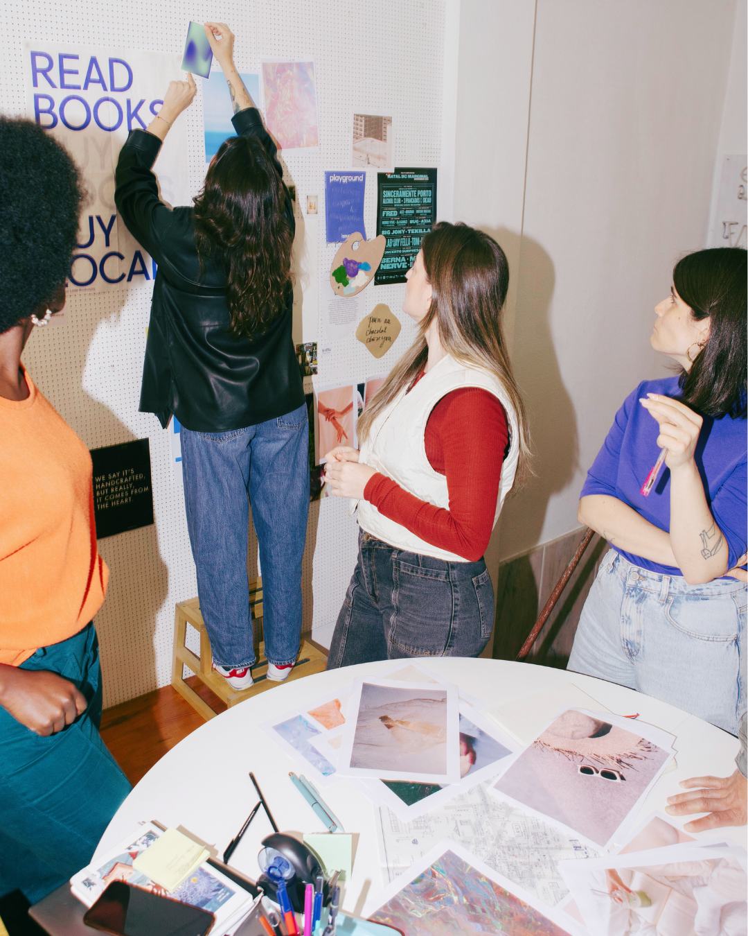 A group of four women stand in front of a moodboard wall during a workshop with visual imagery pens and paper around to be added to the wall
