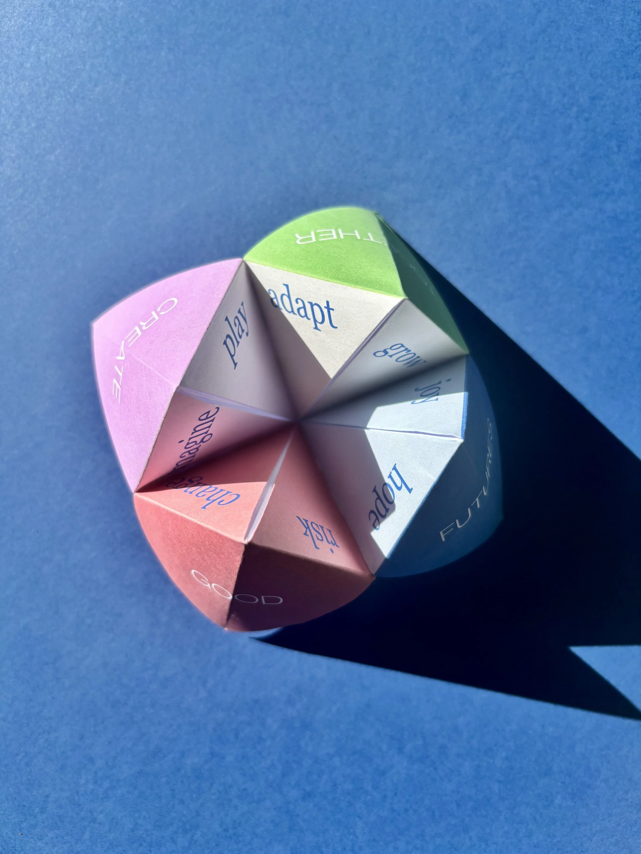 Colorful paper folded into a spiral with words like 'play', 'adapt', and 'grow' written on the sections, placed on a blue background.