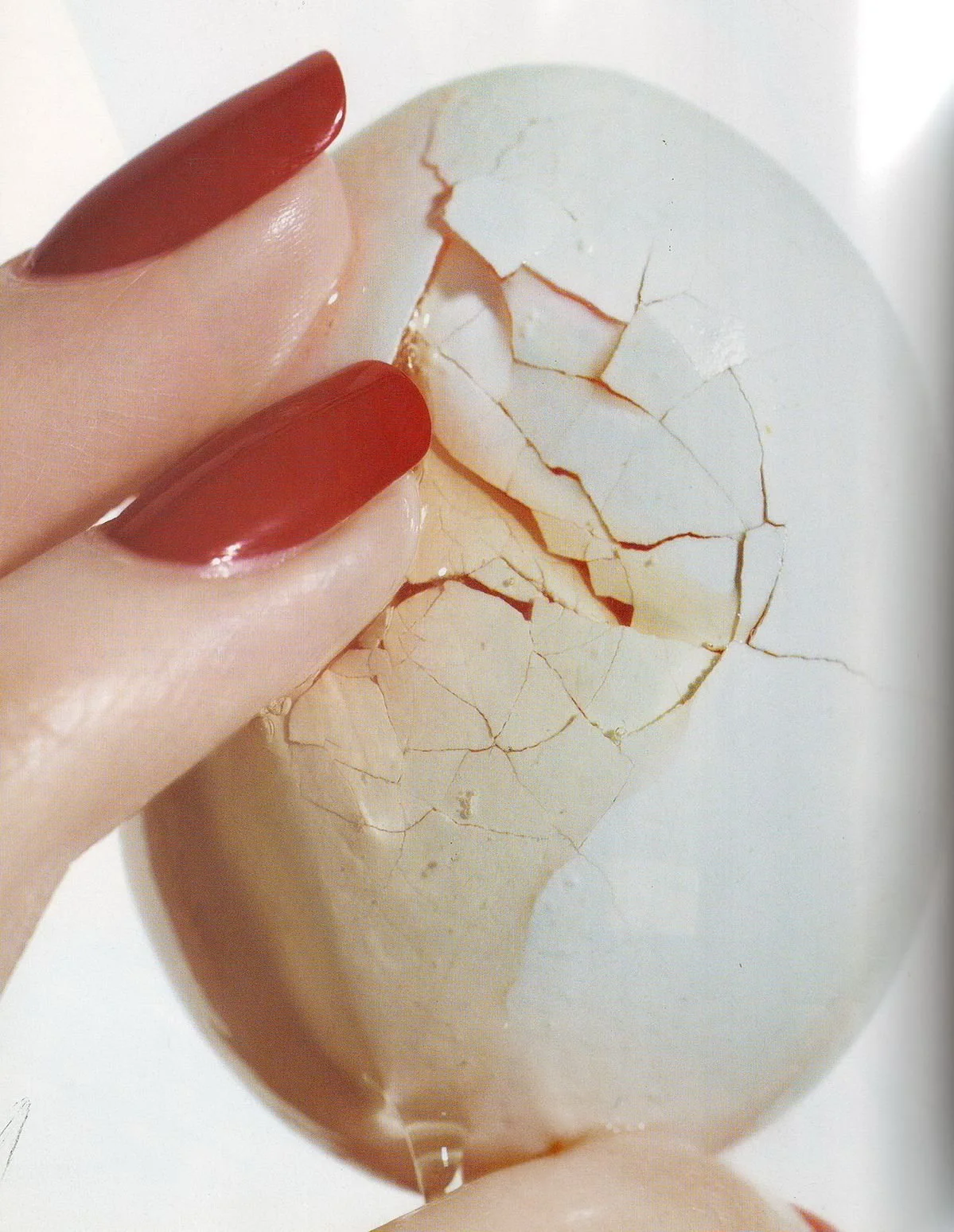 A person's hand with painted red nails holding a cracked eggshell.