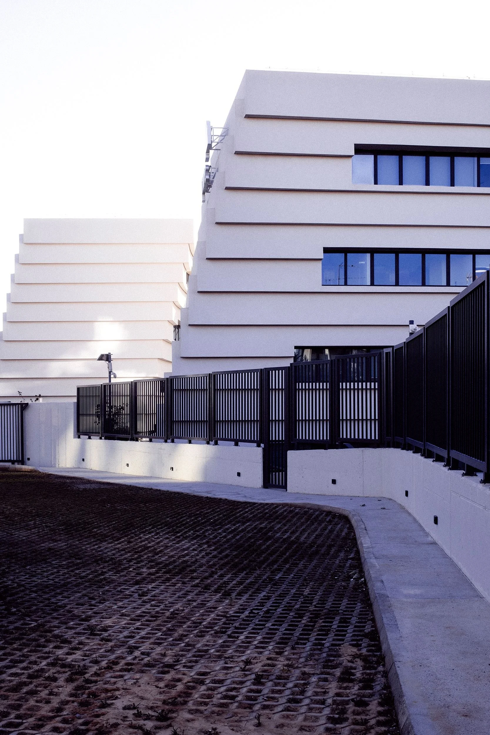 Modern white building with large windows and a black fence in the foreground.