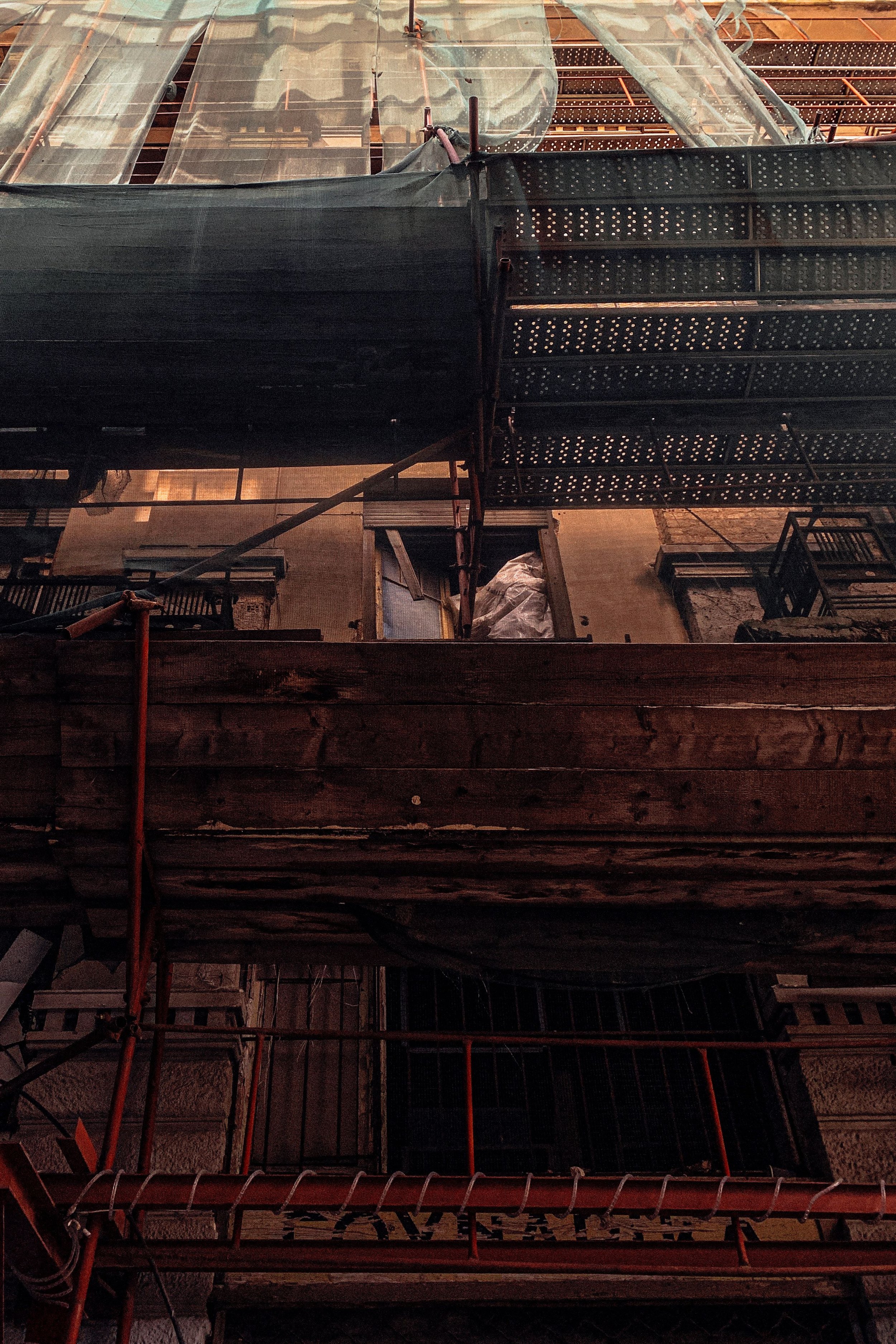View of a building under construction with scaffolding, green netting, and construction materials.