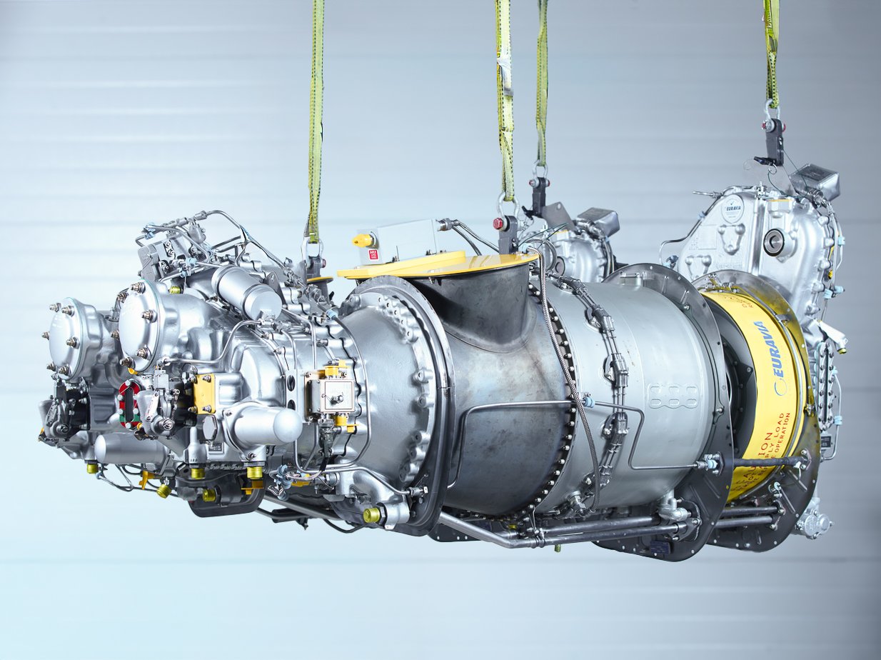A large jet engine suspended from yellow straps against a light blue background.