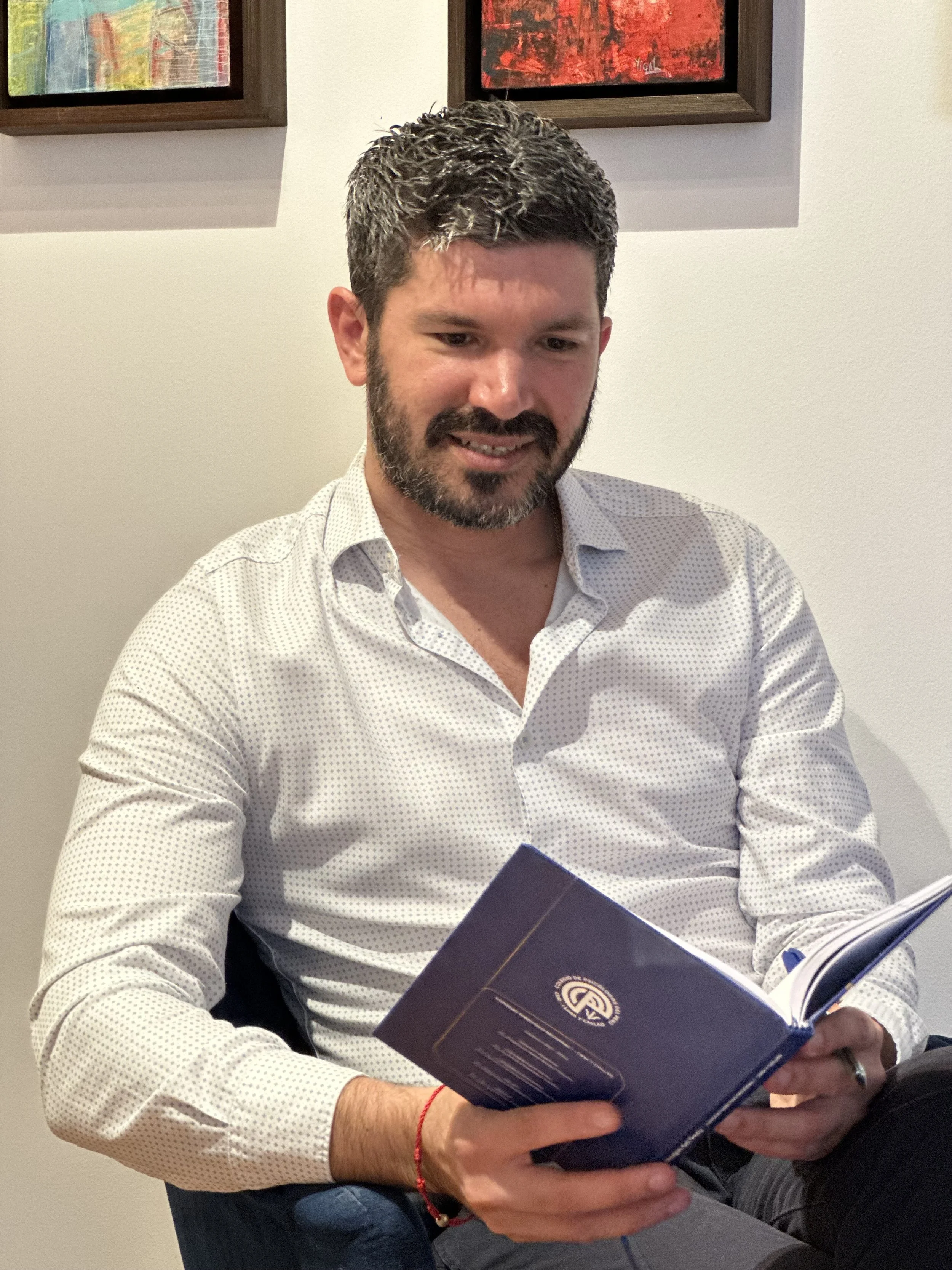 Psicólogo terapeuta hombre, sentado leyendo un texto, con ligera sonrisa, con camisa y pantalón de vestir