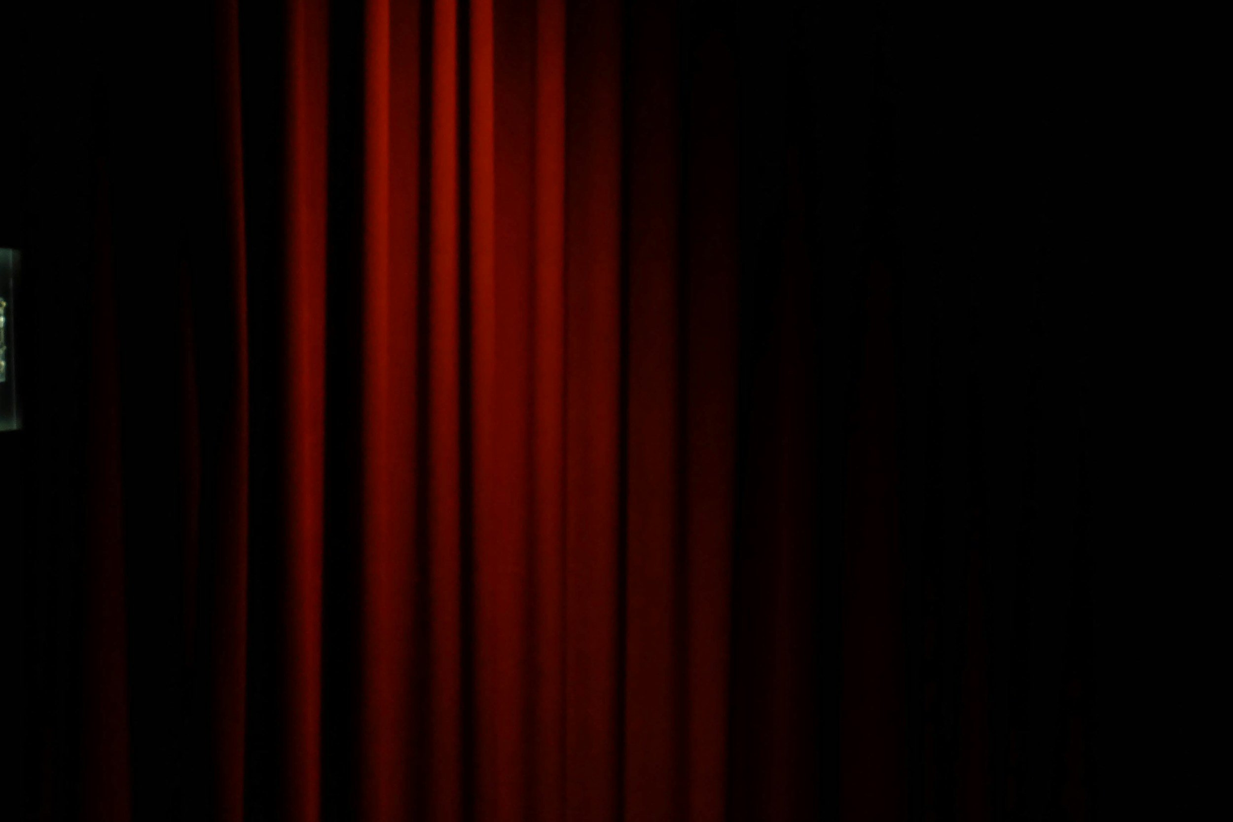 A stock photo of a closed theater curtain peeking out from shadows.