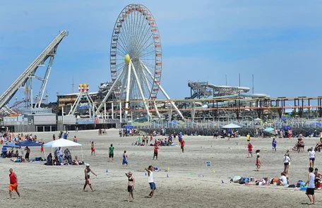 People enjoying the beach with the Santa Monica Pier and Ferris wheel in the background.