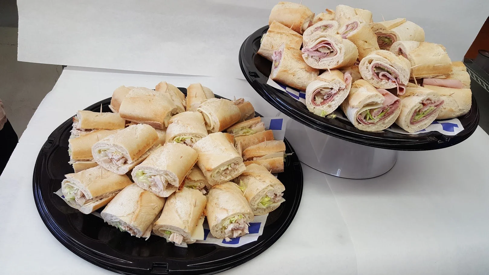 Platters of turkey and lettuce wraps with white bread and various deli meats and vegetables, displayed on black trays.