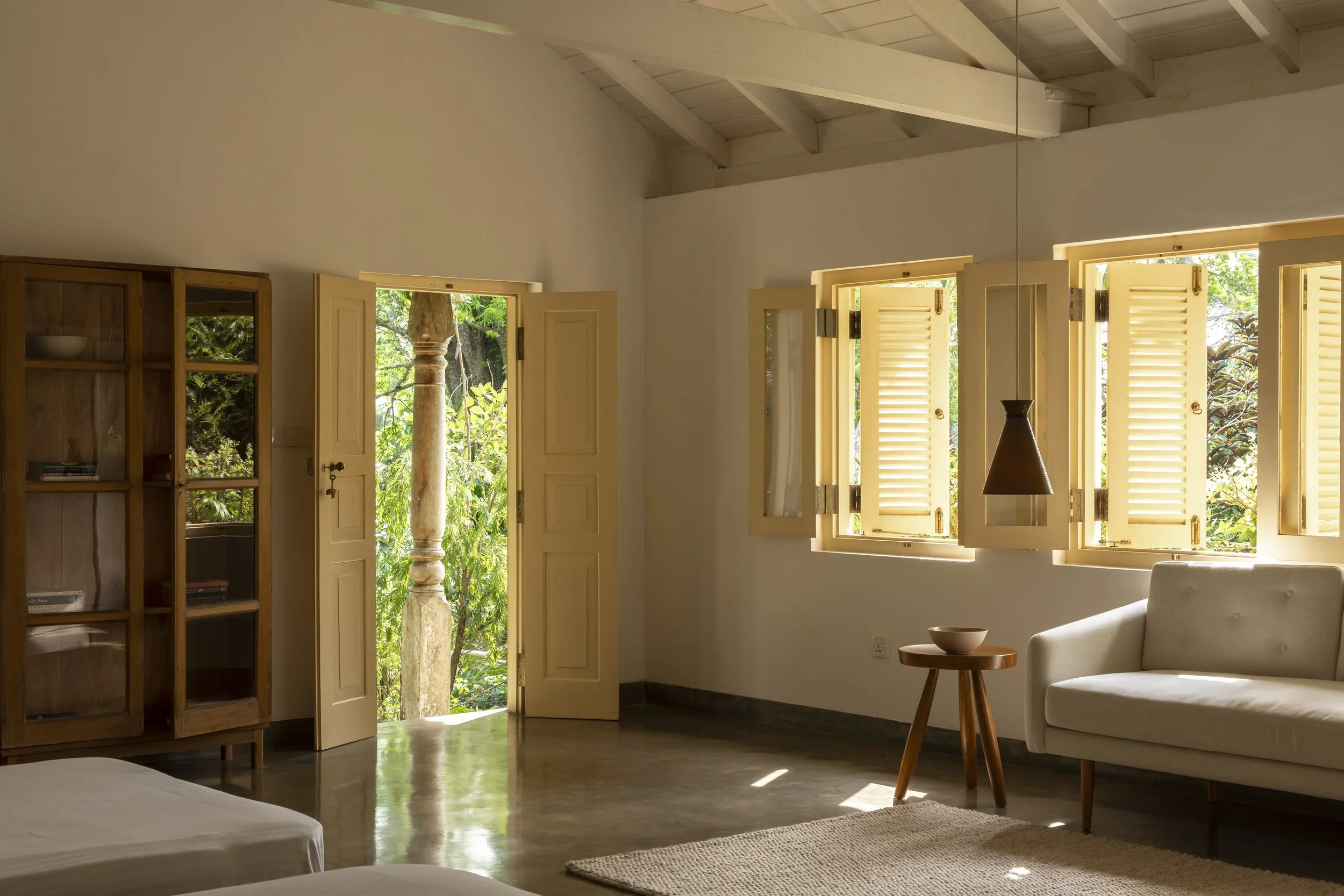 Living room with open windows and door, wooden bookshelf, white sofa, small wooden table, and natural light.