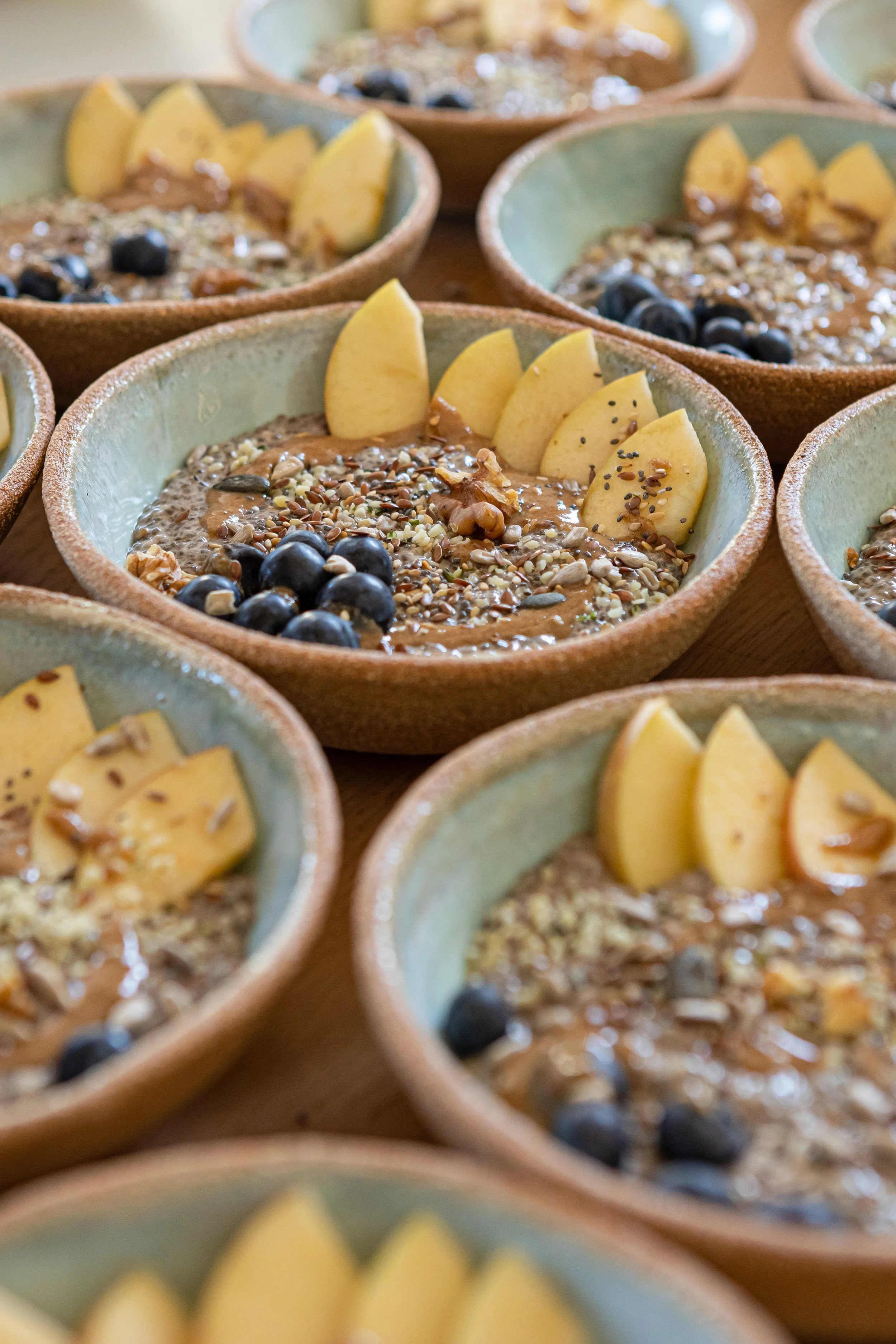 Multiple bowls containing smoothies topped with sliced peaches, blueberries, and mixed seeds.
