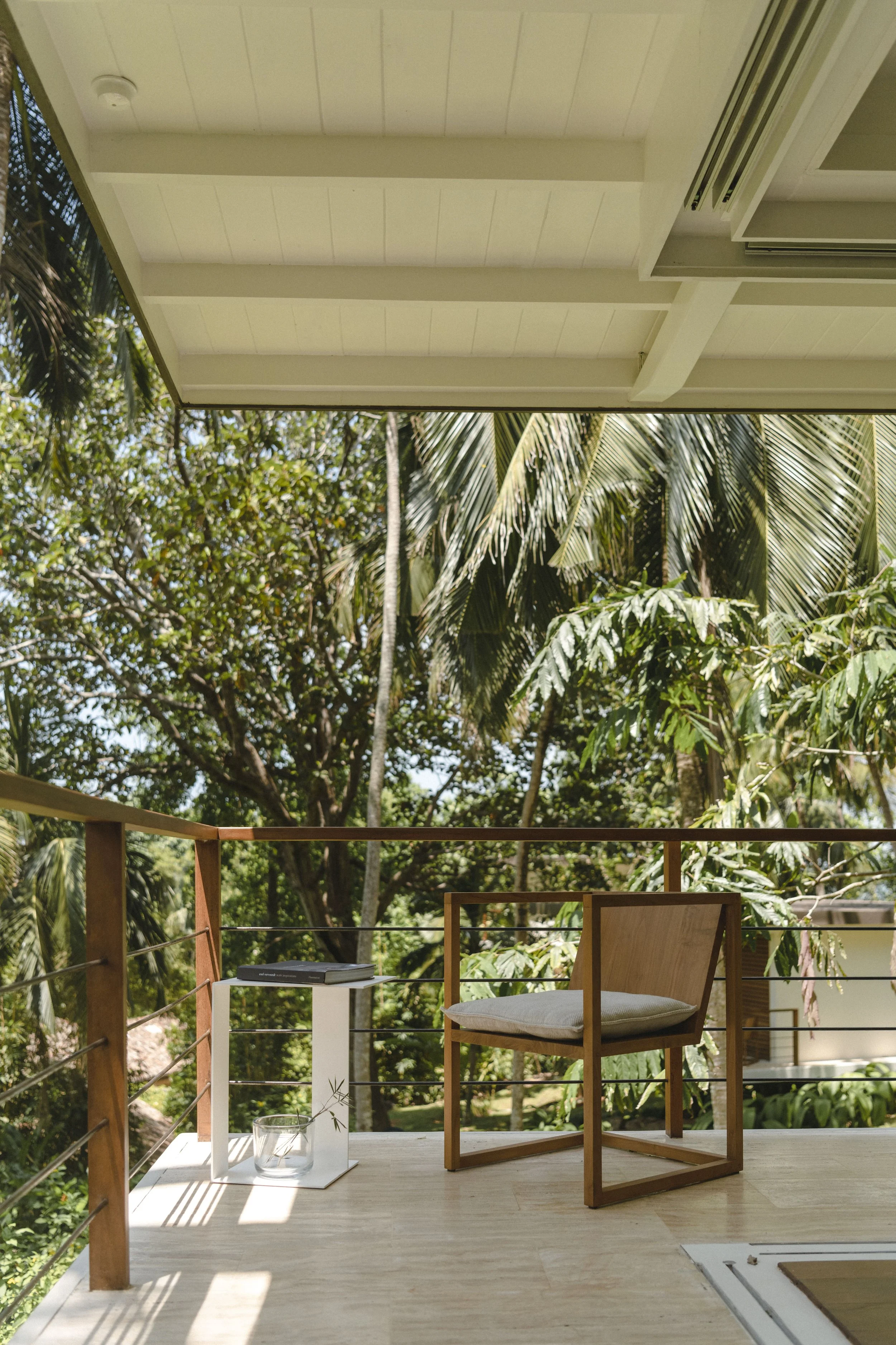 A lakeside view with palm trees, a grassy area, and a small wooden house on stilts with a balcony, shaded by trees.