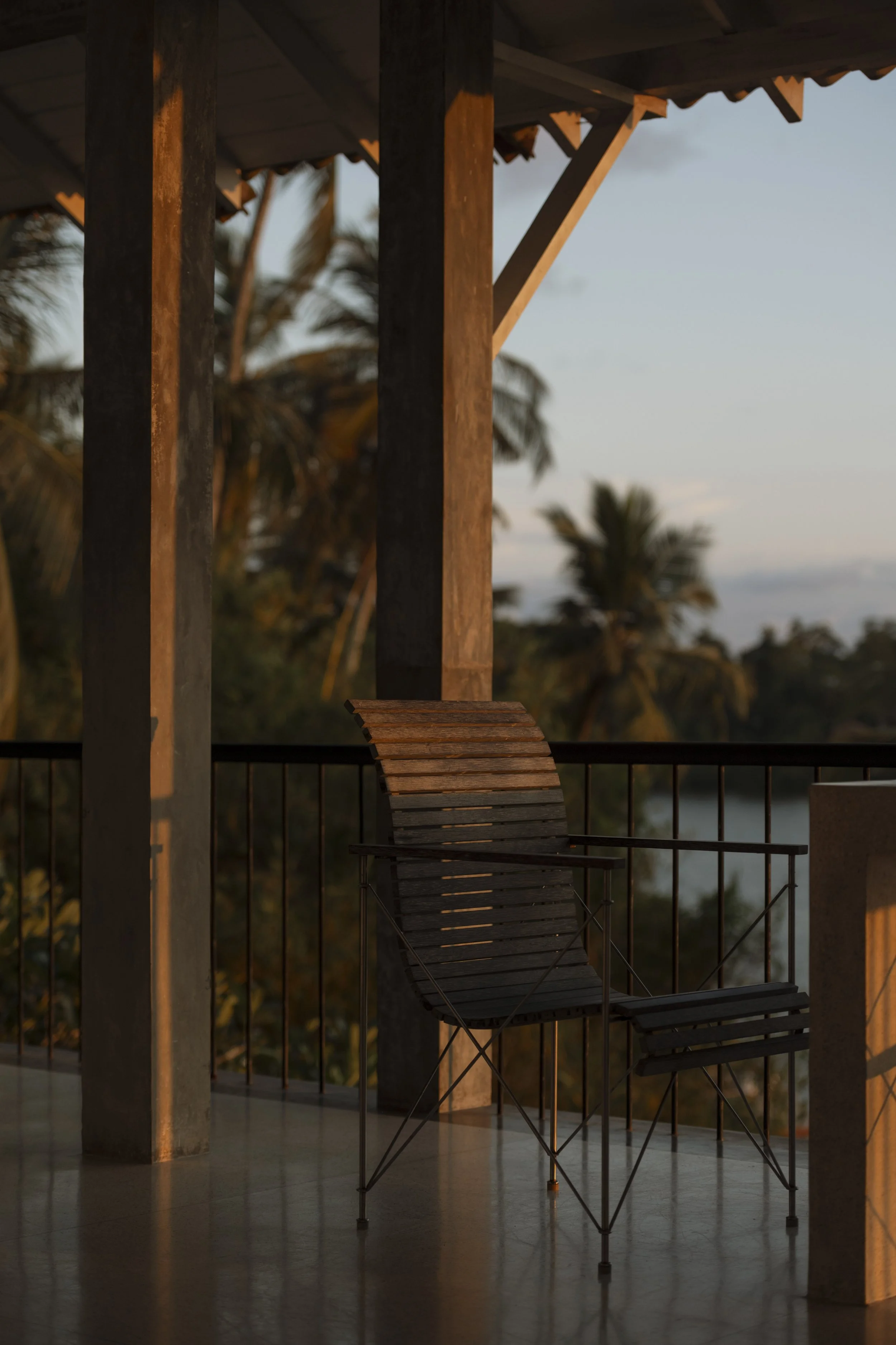 Wooden balcony chair with palm trees in the background during sunset.