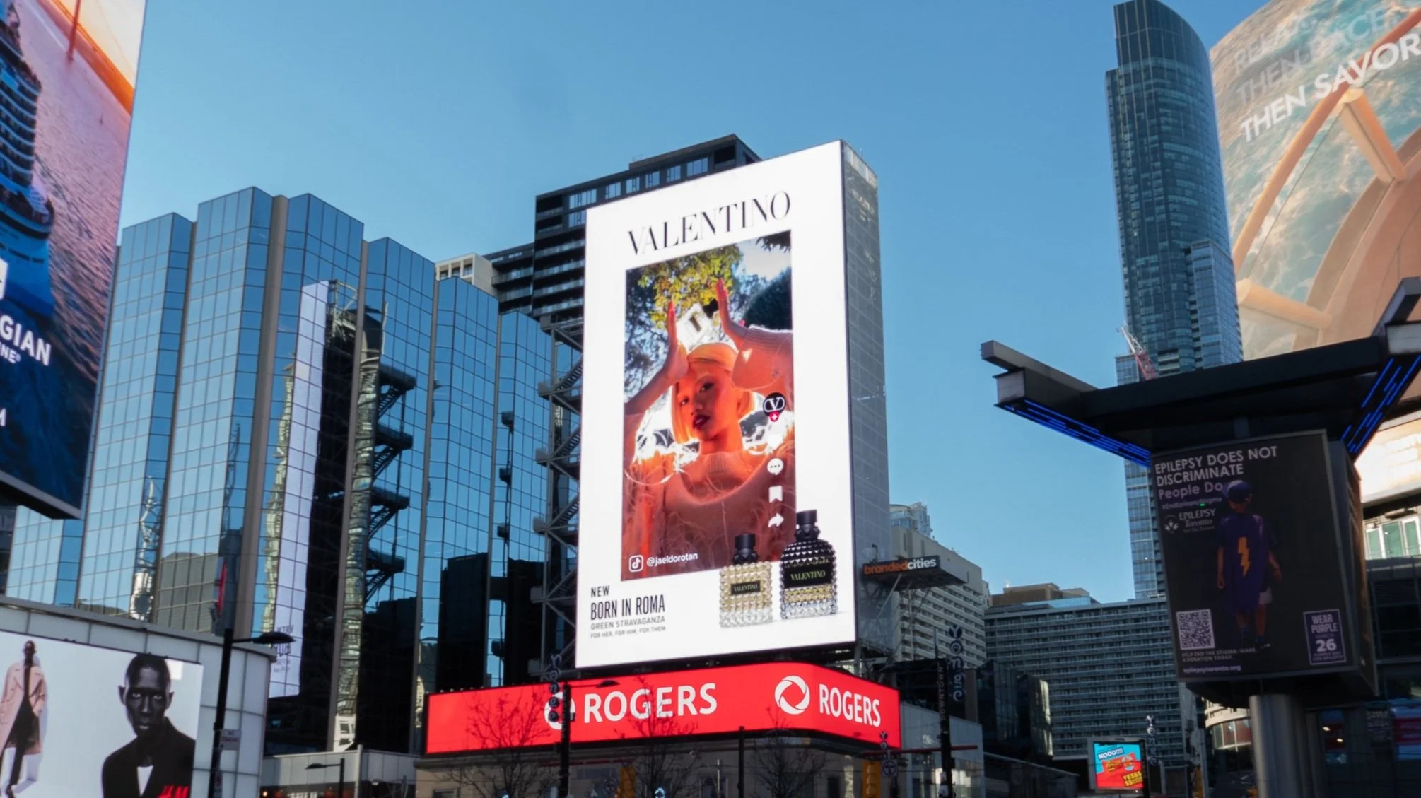 Valentino billboard ad in urban cityscape with modern buildings, Rogers logo, and other advertisements.