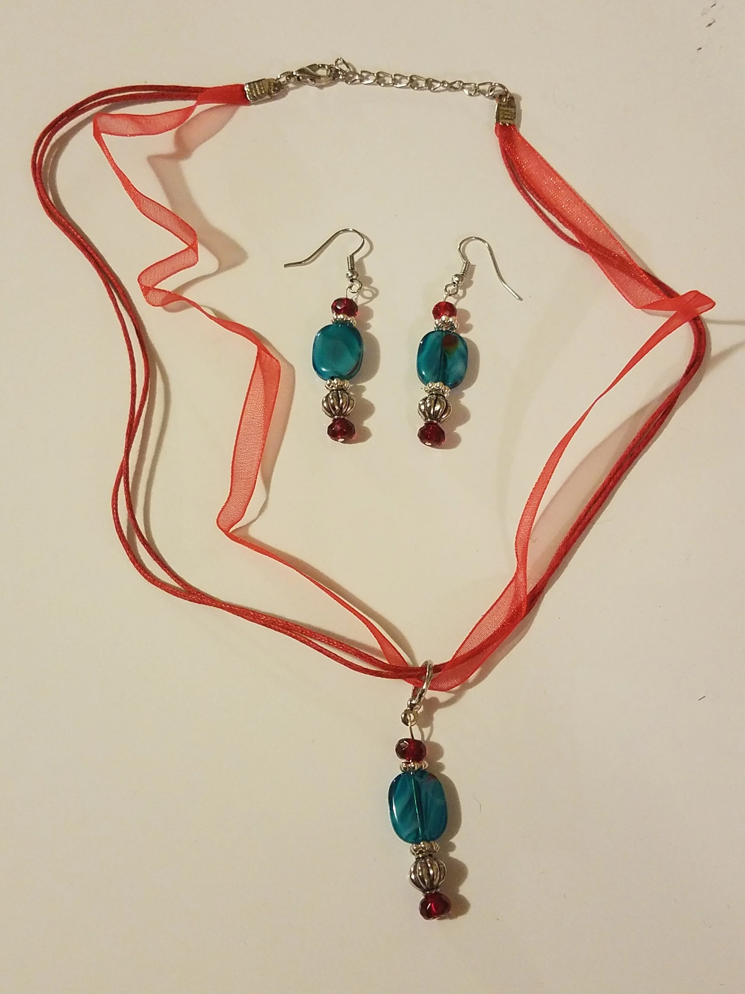 A jewelry set consisting of a red ribbon choker with a pendant, and matching earrings with blue and red beads.
