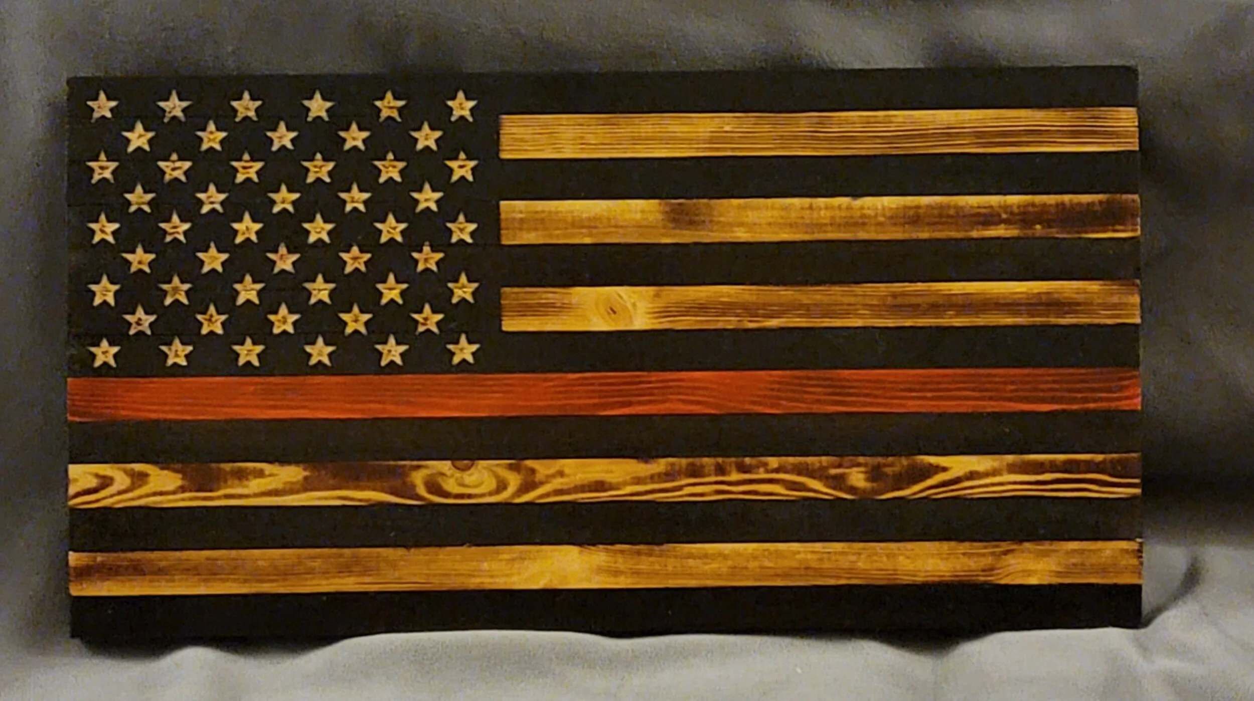 Wooden American flag wall art with black, natural, and red stripes and white stars on a black background.