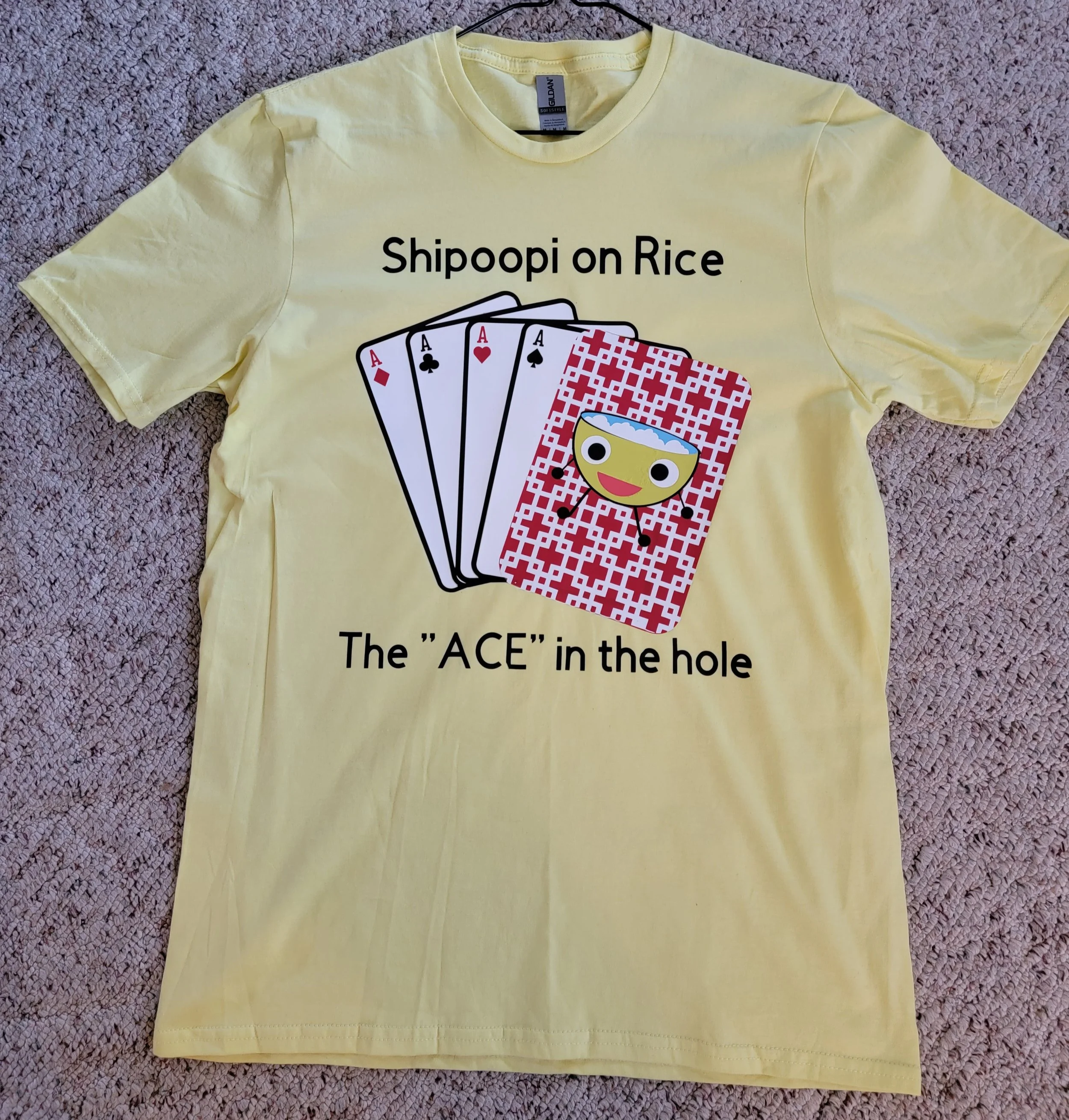Yellow T-shirt with a design of playing cards and a rice-themed character, with text 'Shipoopi on Rice The 'ACE' in the hole'.