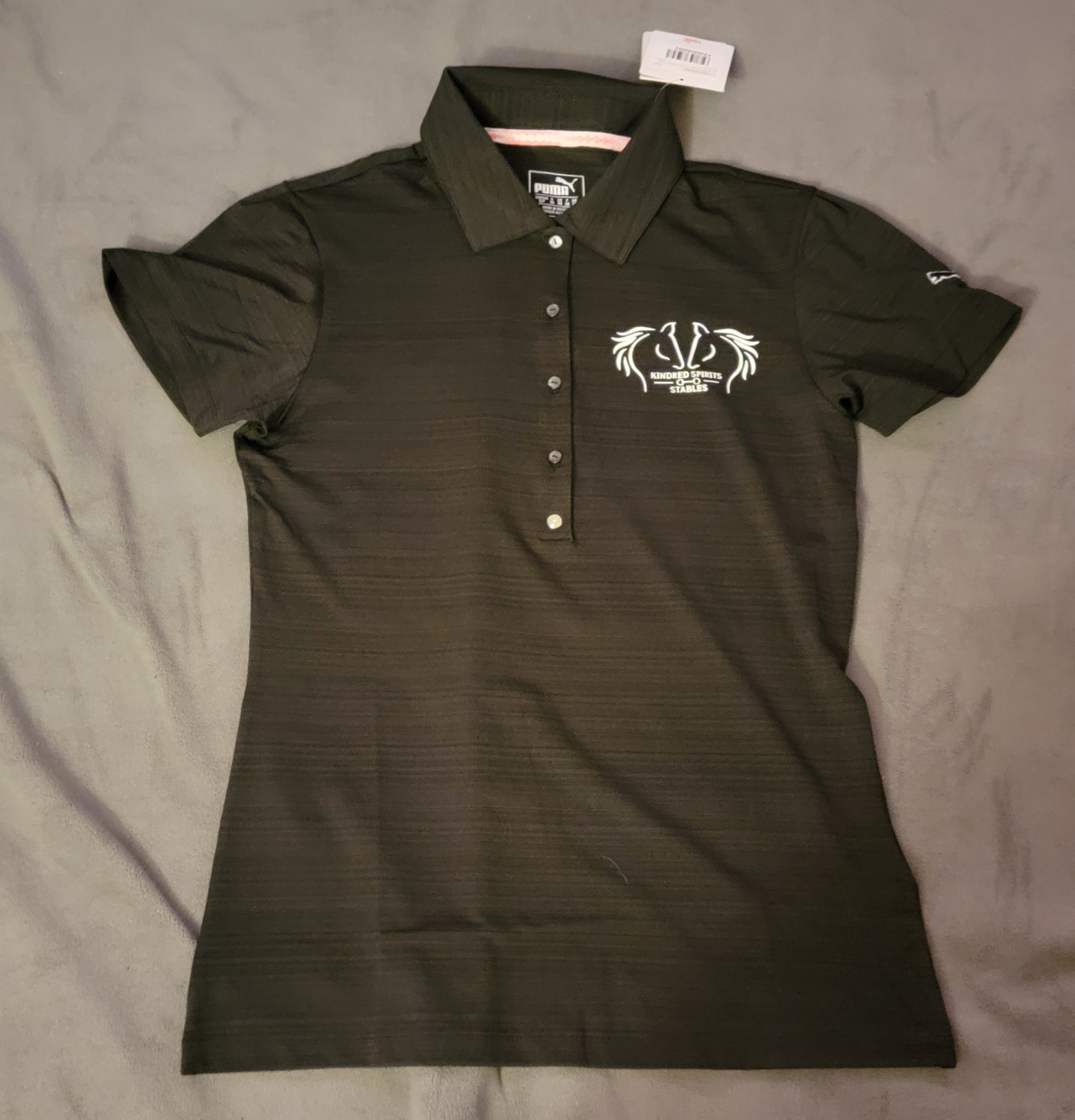 Black short-sleeve polo shirt with a logo on the left chest that reads 'Kindred Spirits Stables' and a small logo on the left sleeve.