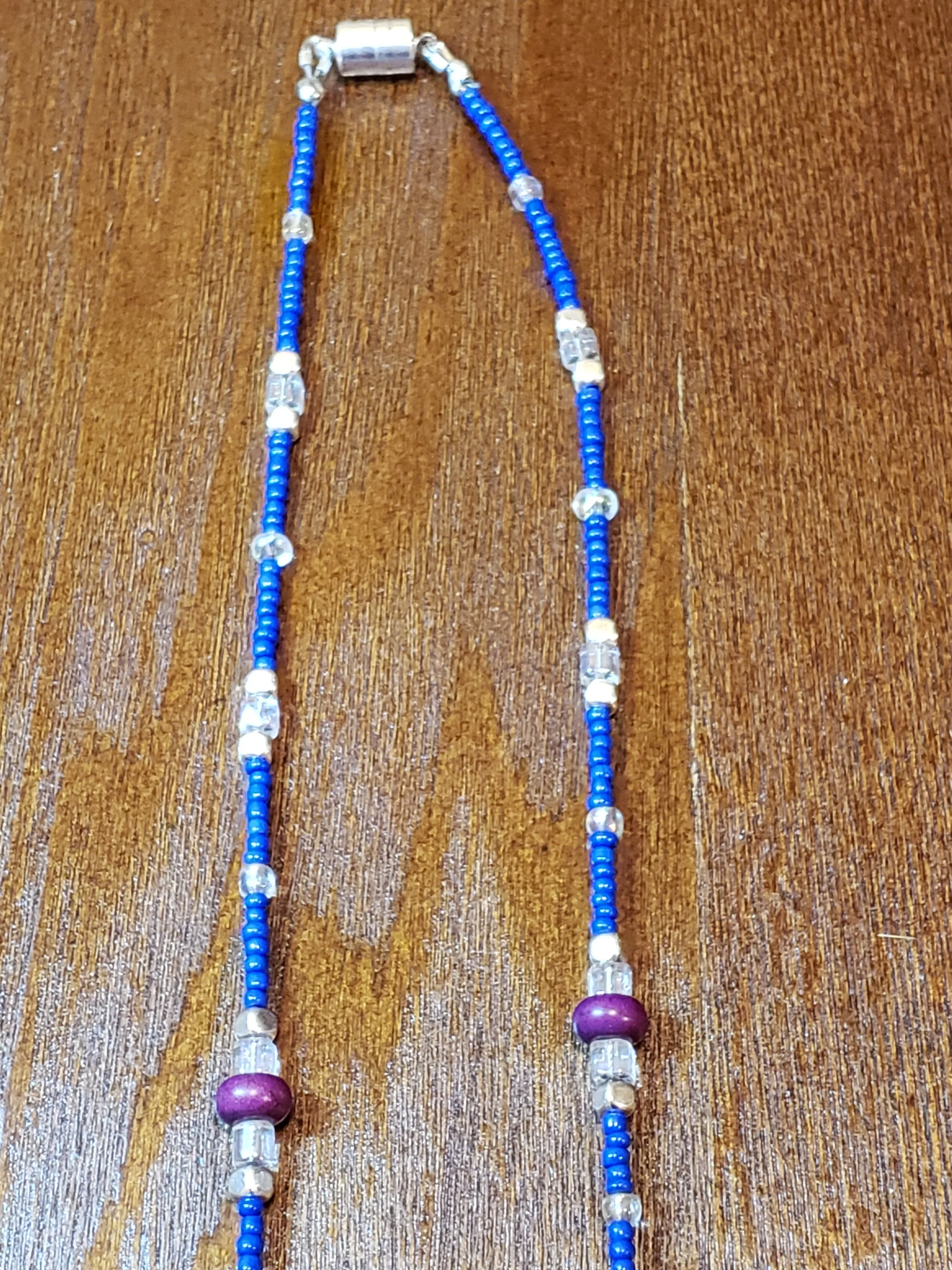 A beaded necklace with blue, clear, purple, and white beads laid out on a wooden surface.