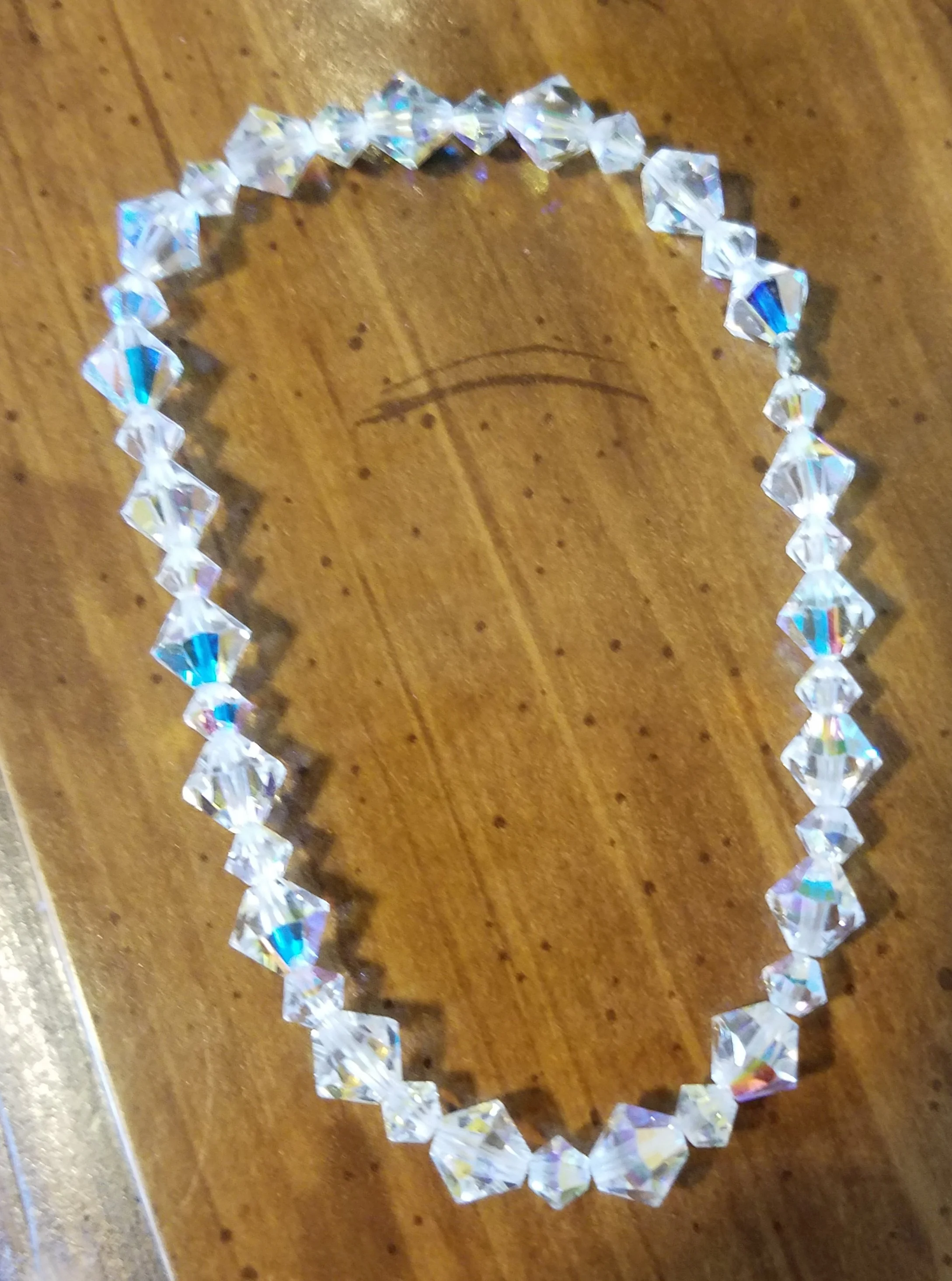 A circle of clear, faceted crystals with a rainbow shine on a wooden surface.