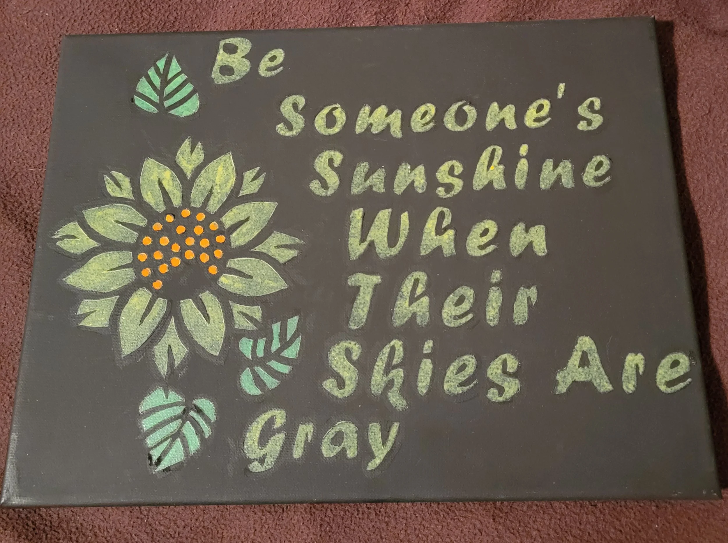 A black canvas with a colorful chalk drawing of a sunflower and green leaves. Next to the sunflower, a quote reads, 'Be someone’s sunshine when their skies are gray' in yellowish-green letters.