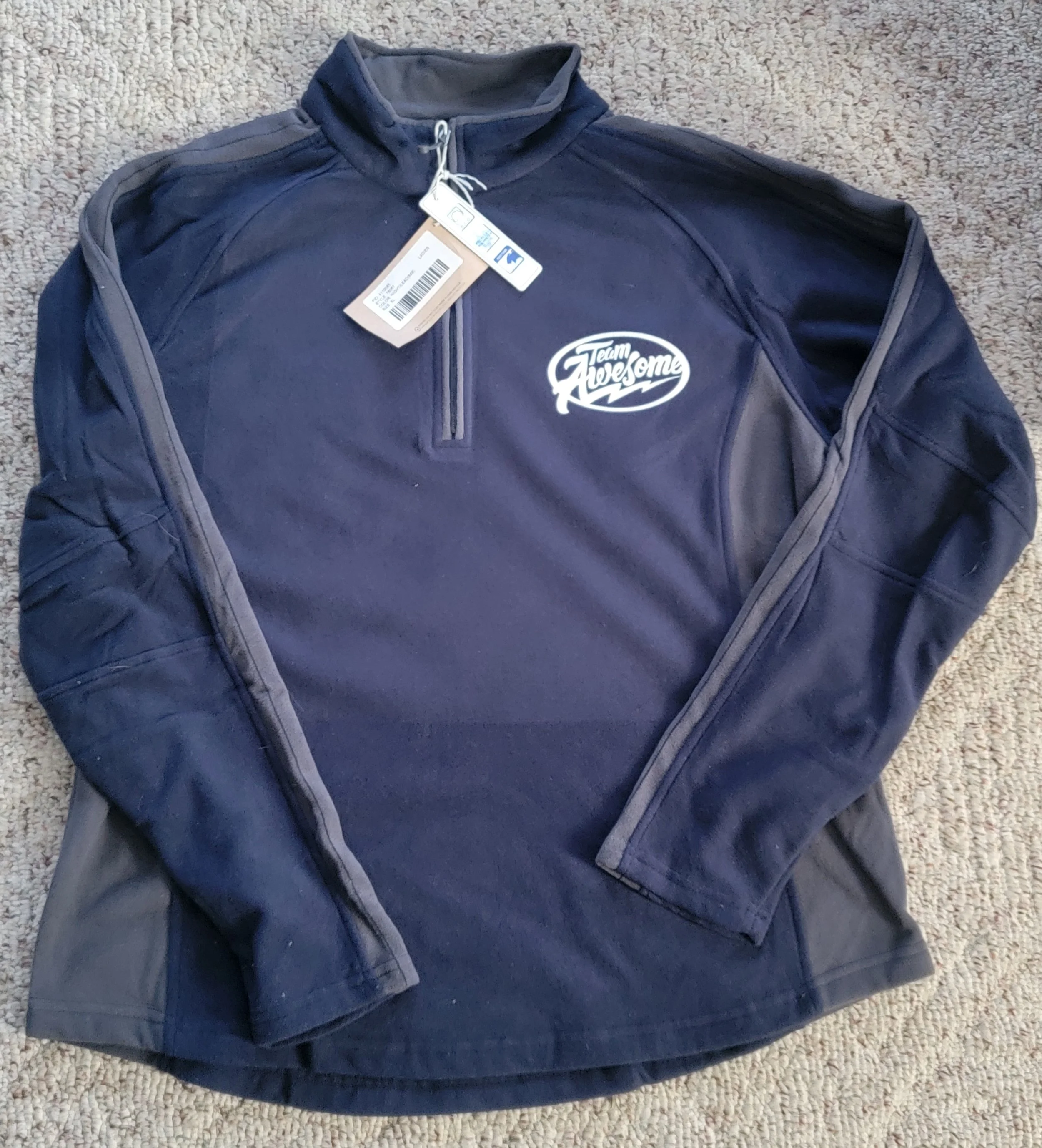 A navy blue athletic pullover with a quarter zip front and the logo 'Team Awesome' on the left chest, lying on a beige carpet.