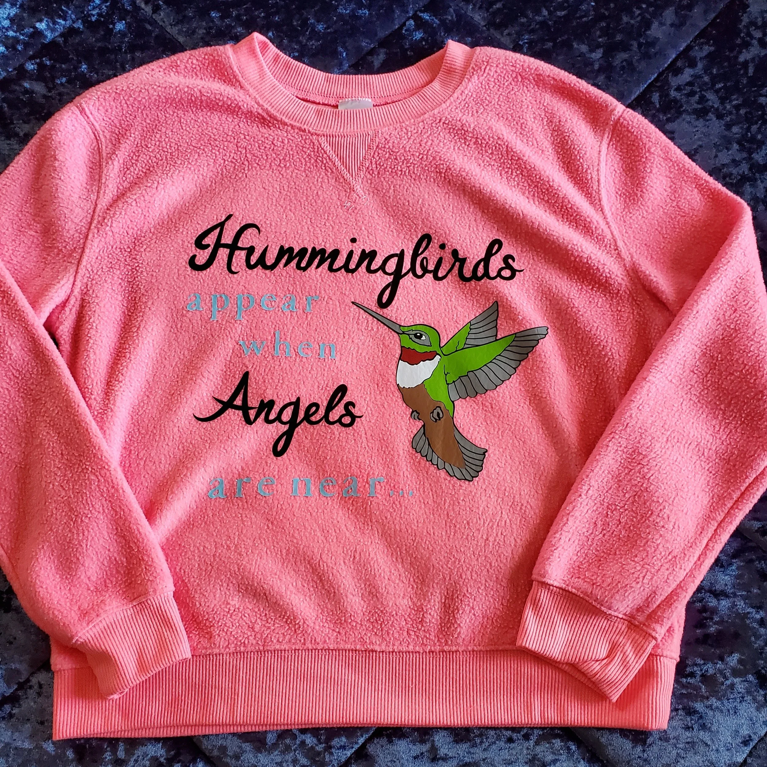 Pink fleece sweatshirt with a hummingbird illustration and the quote, 'Hummingbirds appear when angels are near...'