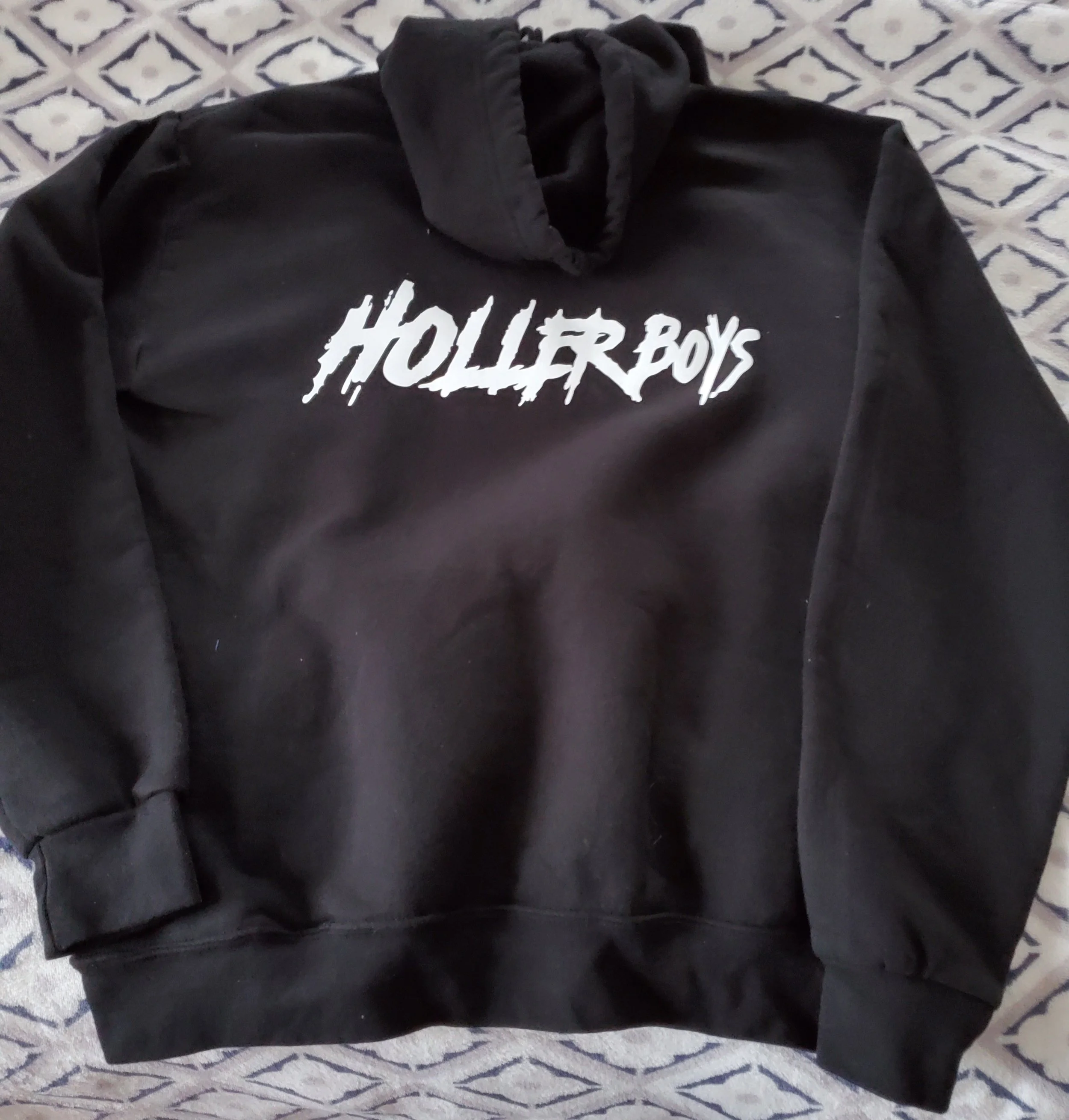 Black hoodie with white 'Holler Boys' text on the front, laid on a patterned surface.