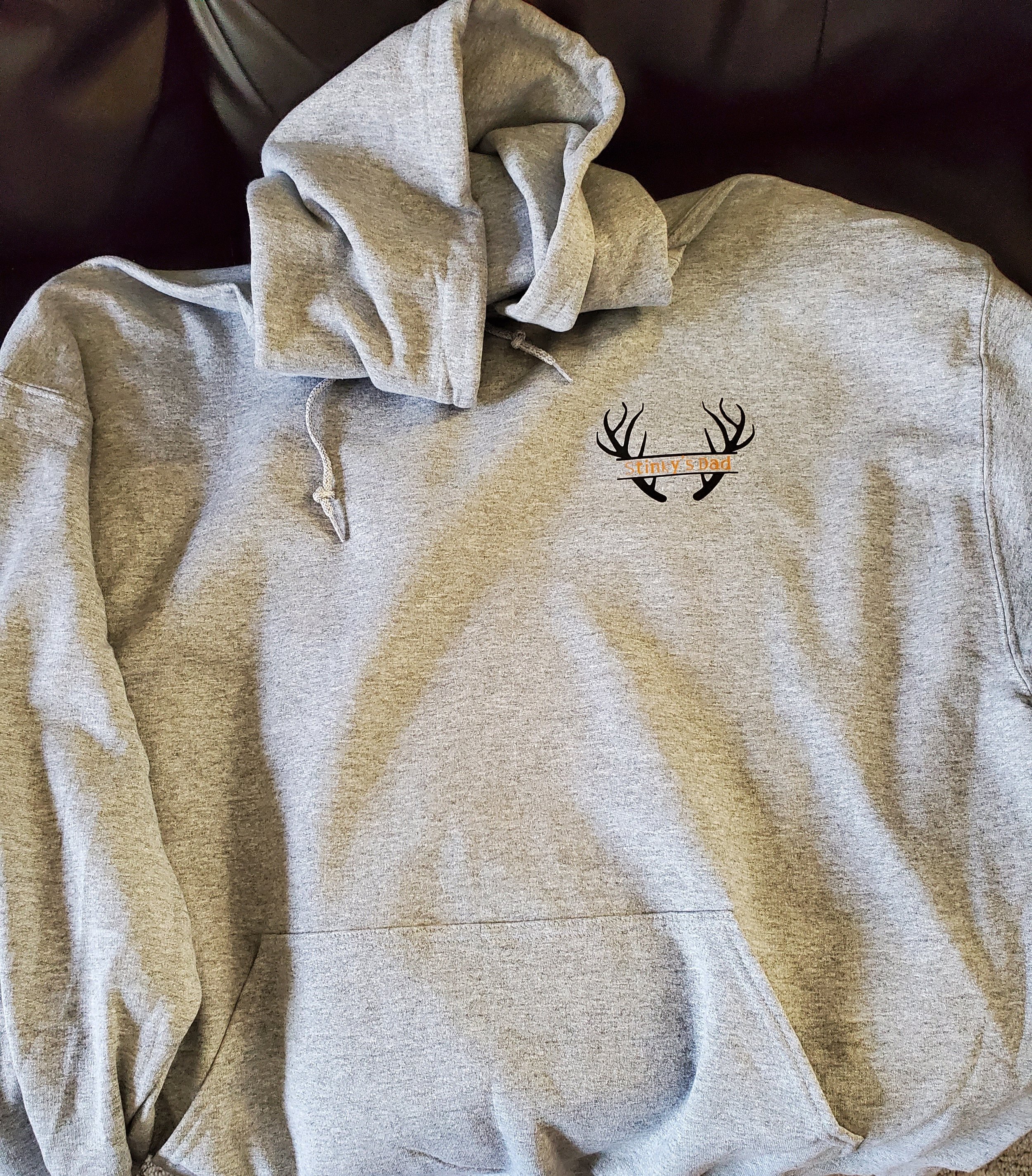 Gray hoodie with a design of antlers and a banner that reads 'Stinky's Dad' on the front.