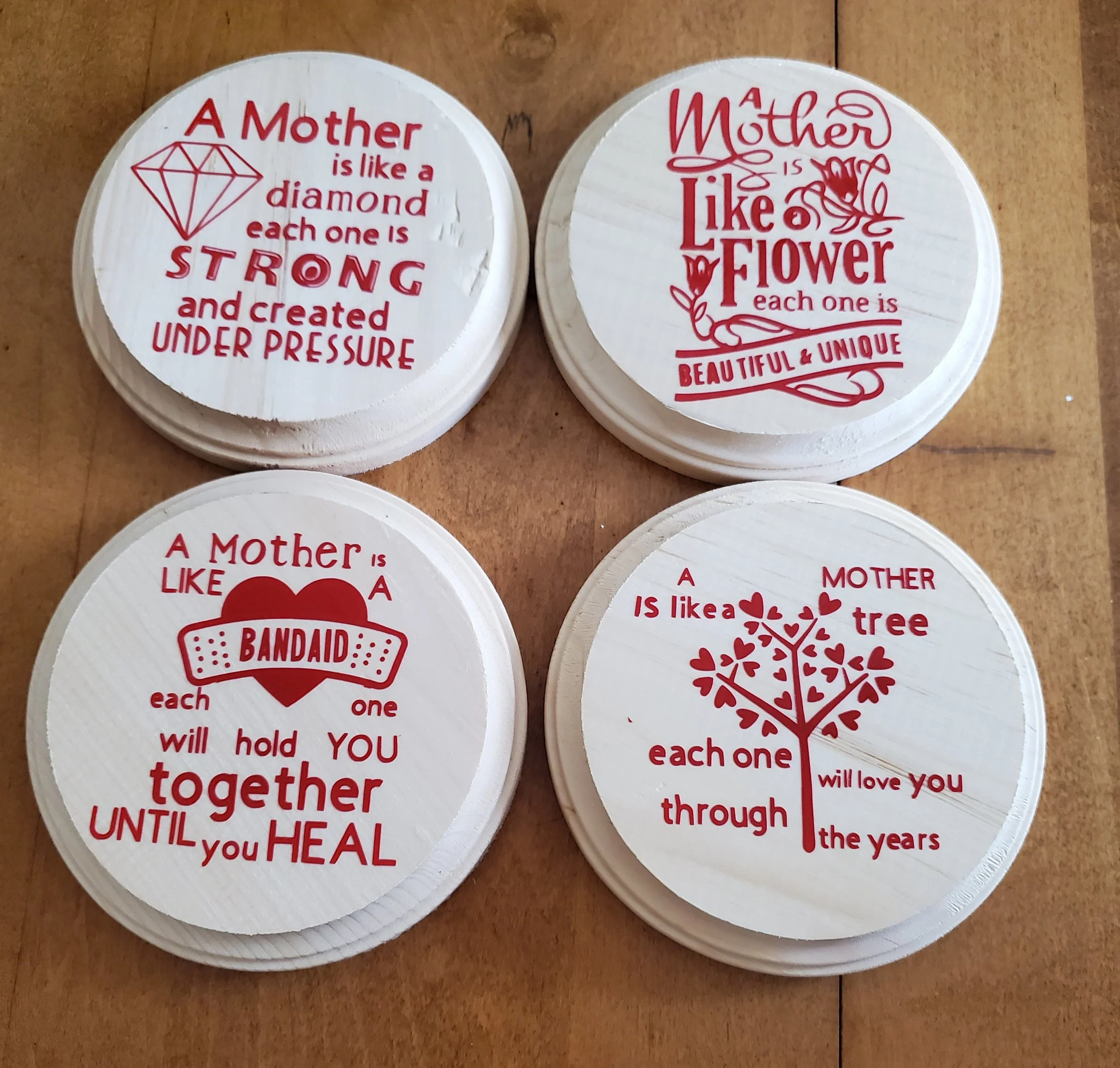 Set of four paper coasters with red inspirational quotes about mothers. One features a diamond graphic and the text, 'A Mother is like a diamond, each one is strong and created under pressure.' Another has a flower graphic with the words, 'A Mother i